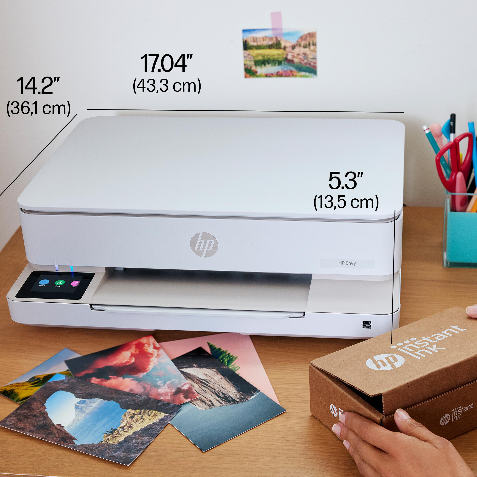 Ein weißer HP Envy Drucker auf einem Holztisch mit gedruckten Fotos und einer Instant Ink Box.