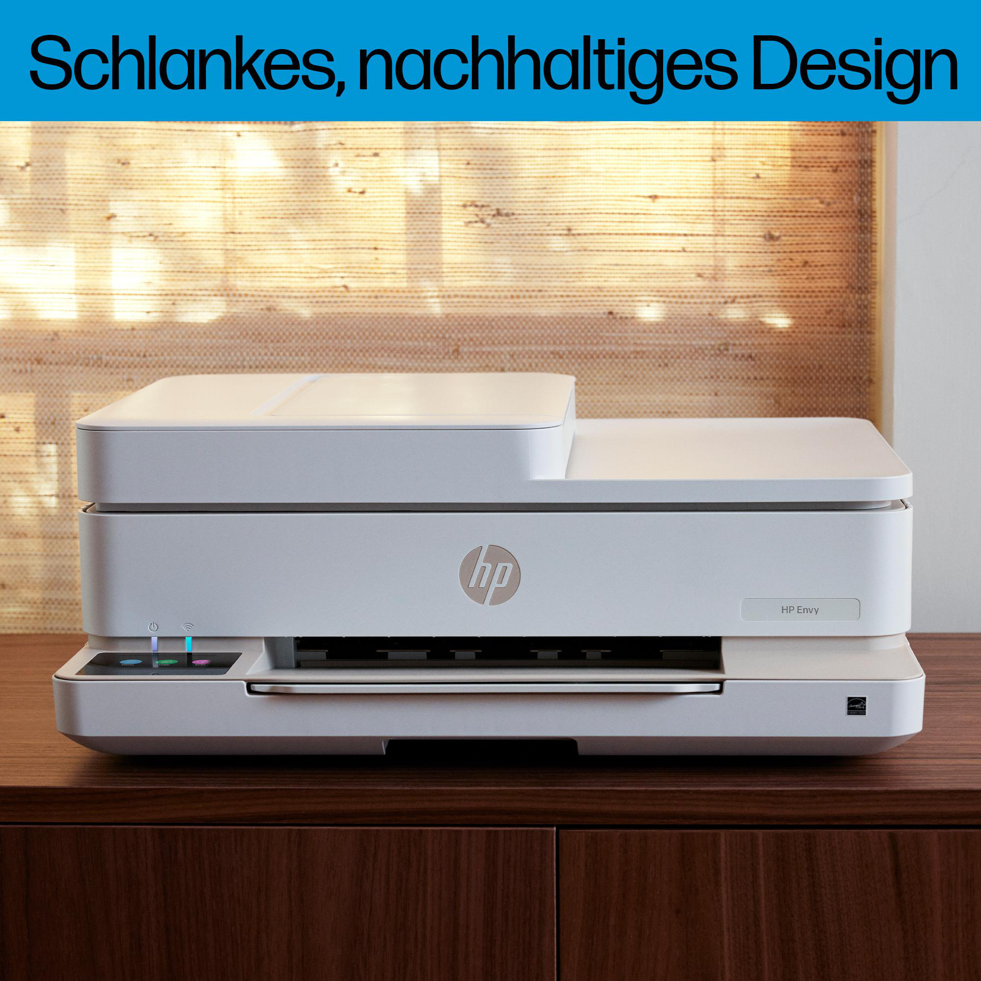 Ein weißer HP Envy Drucker steht auf einem dunklen Holzschrank vor einem Fenster mit Jalousie.