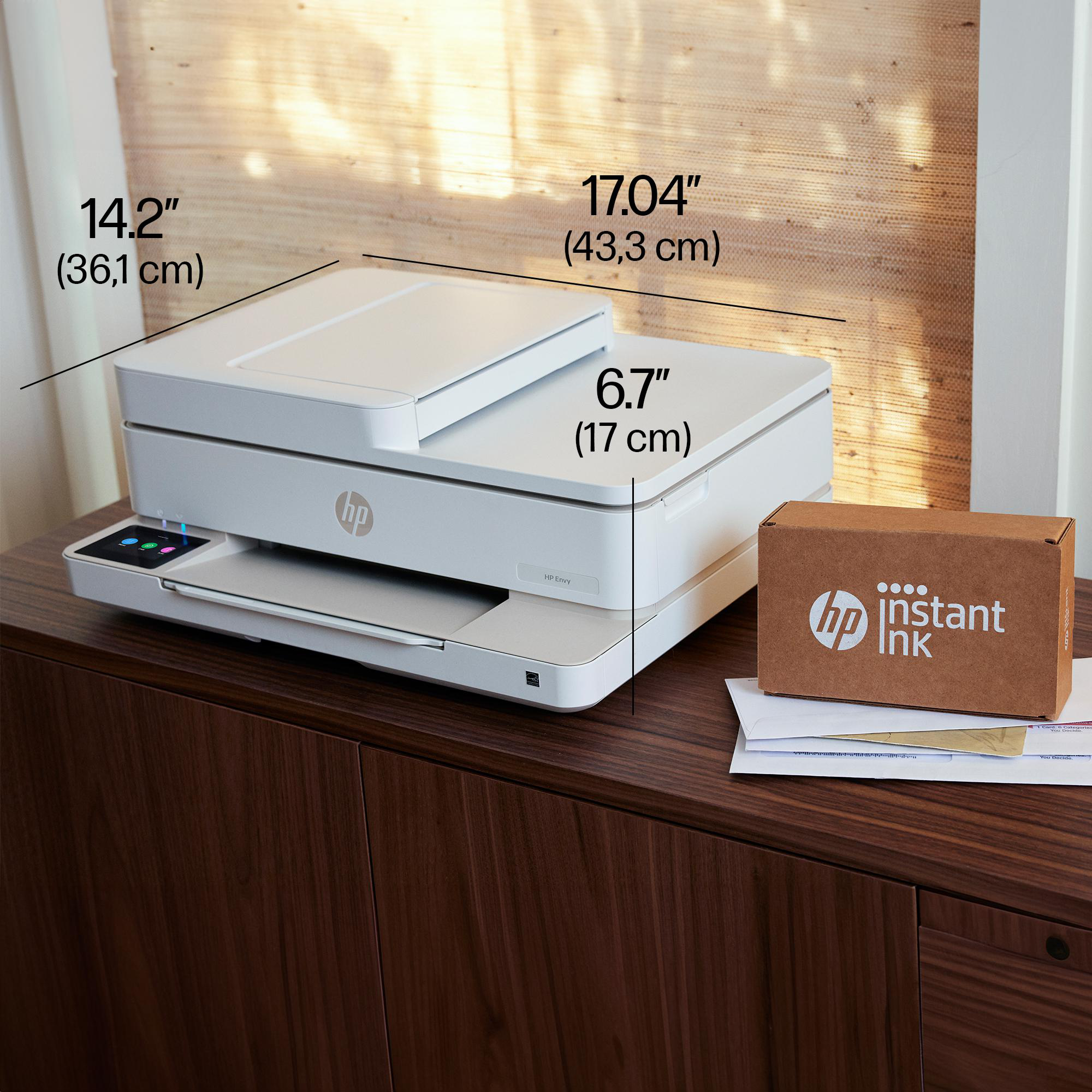 Weißer HP Envy Drucker auf braunem Schrank mit Maßen und kleiner HP Instant Ink Box daneben.