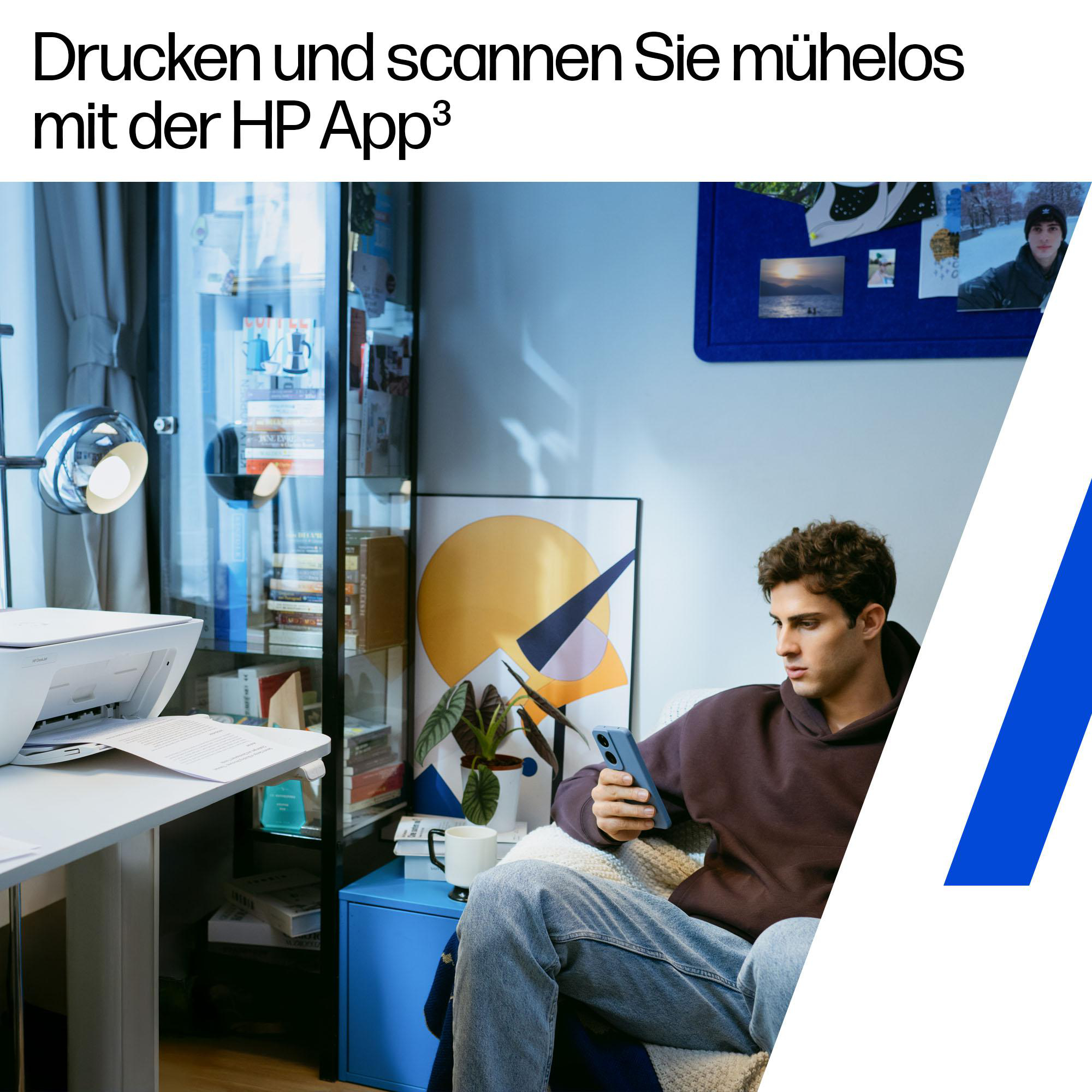 Ein Mann sitzt in einem gemütlichen Zimmer mit Drucker, Regal und Handy.