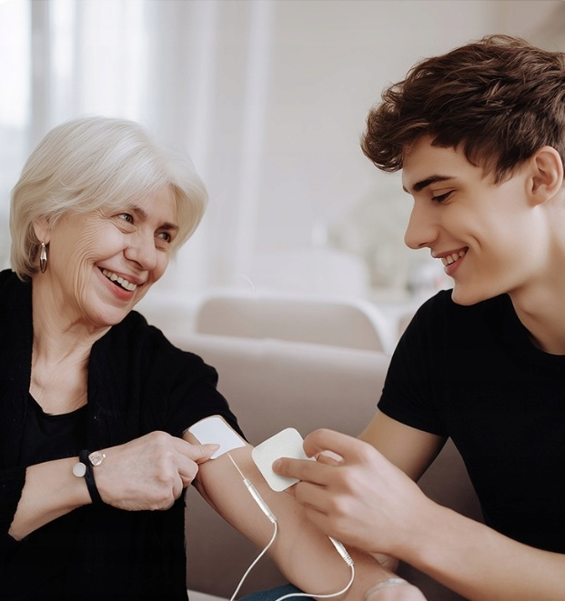 Młody mężczyzna pomaga starszej kobiecie nakleić elektrody na ramię.