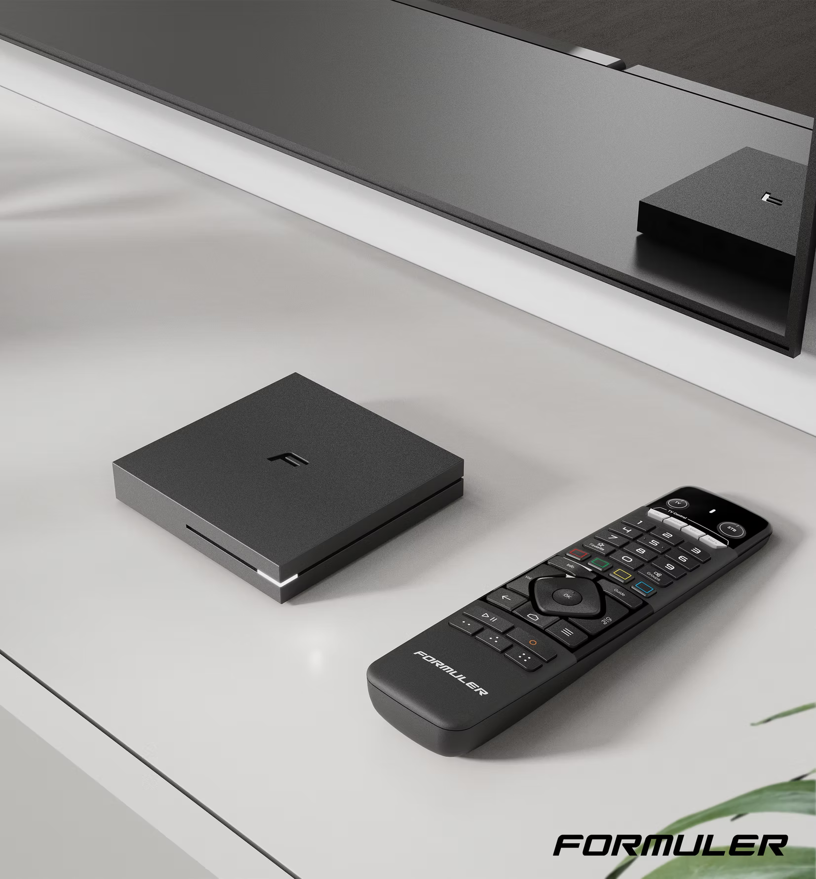 Un box streaming e un telecomando Formuler neri poggiano su una superficie bianca con uno schermo scuro.