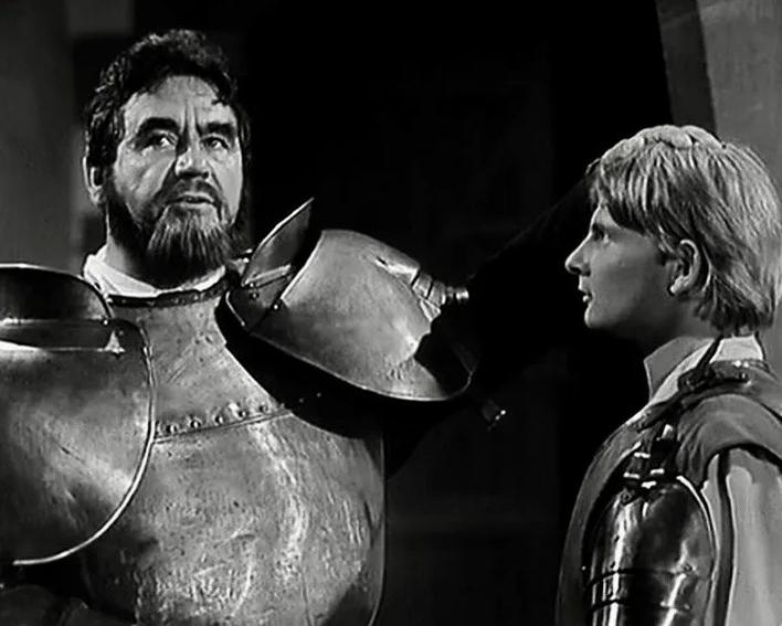Ein schwarz-weißes Bild zeigt einen Ritter mit Bart und Rüstung im Gespräch mit einem jungen Knappen.