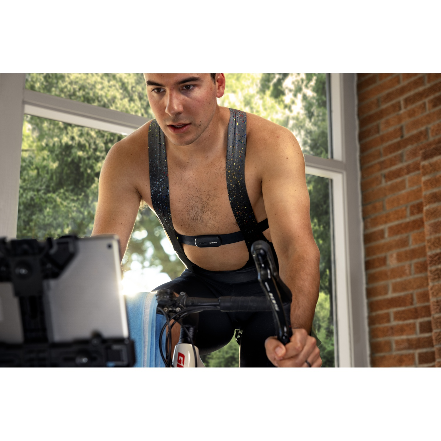 Een man fietst binnenshuis op een hometrainer met een tablet voor zich, dragend in koersbroek.