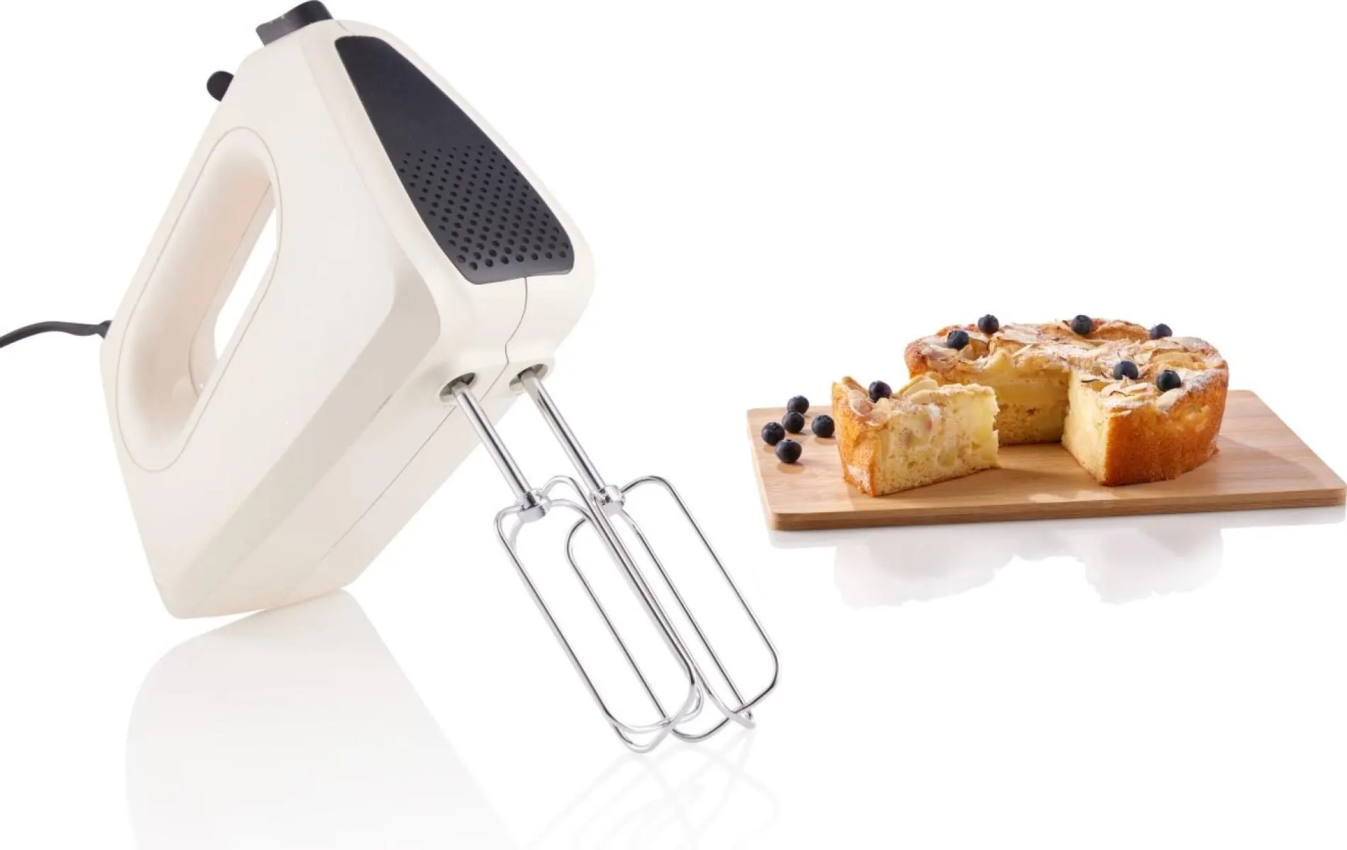 Egy fehér kézi mixer és egy szeletelt áfonyás almatorta egy fa vágódeszkán, fekete háttér előtt.