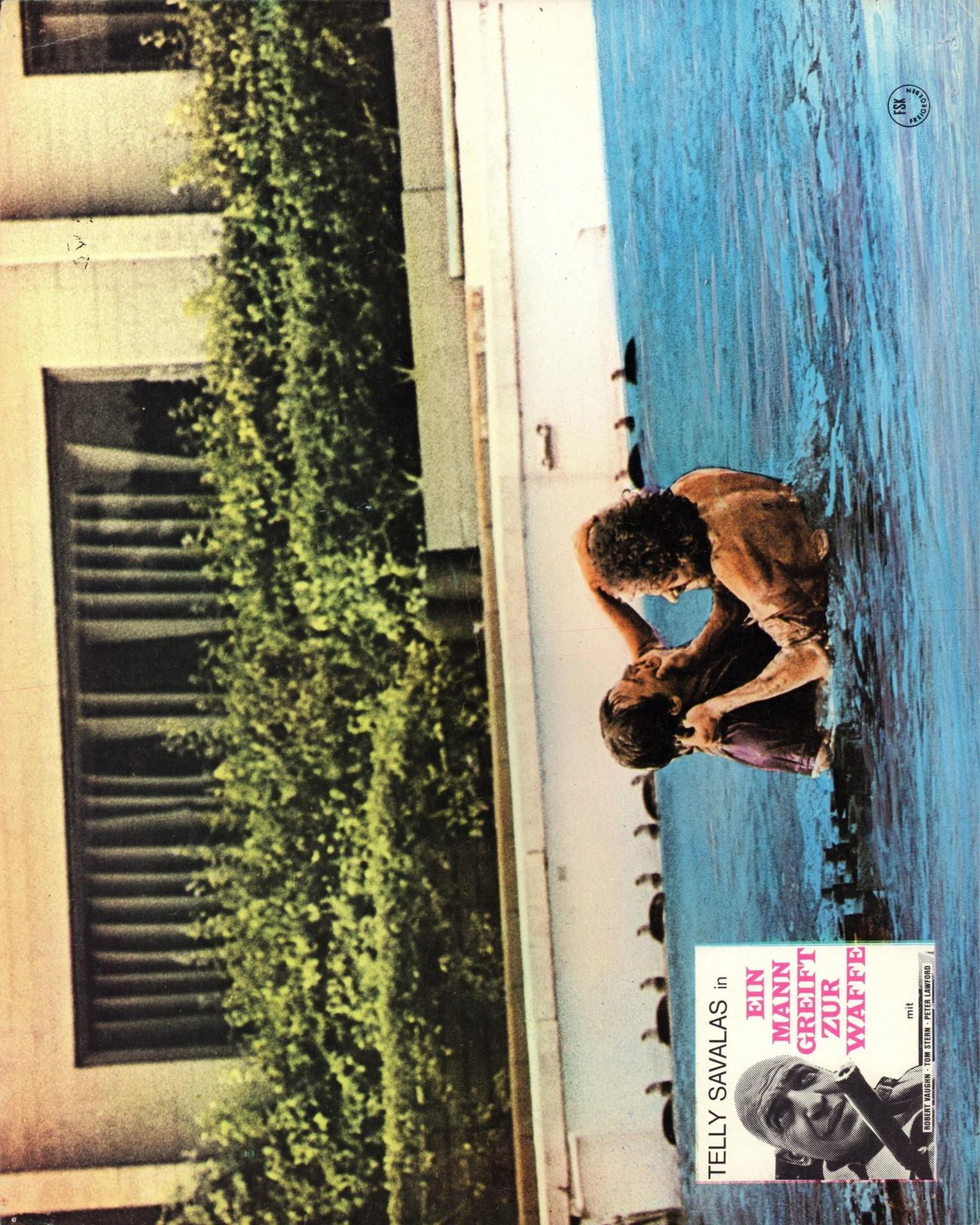 Zwei Männer kämpfen in einem Swimmingpool neben einem Gebäude mit grünen Büschen und einem Filmposter.