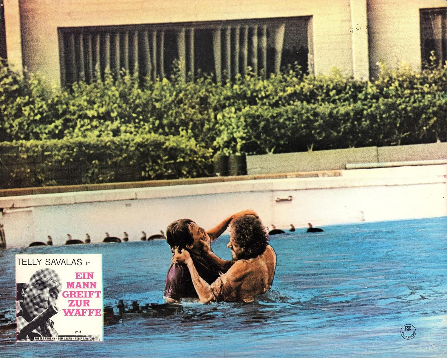 Zwei Männer kämpfen in einem Swimmingpool, im Hintergrund ist ein Gebäude zu sehen.