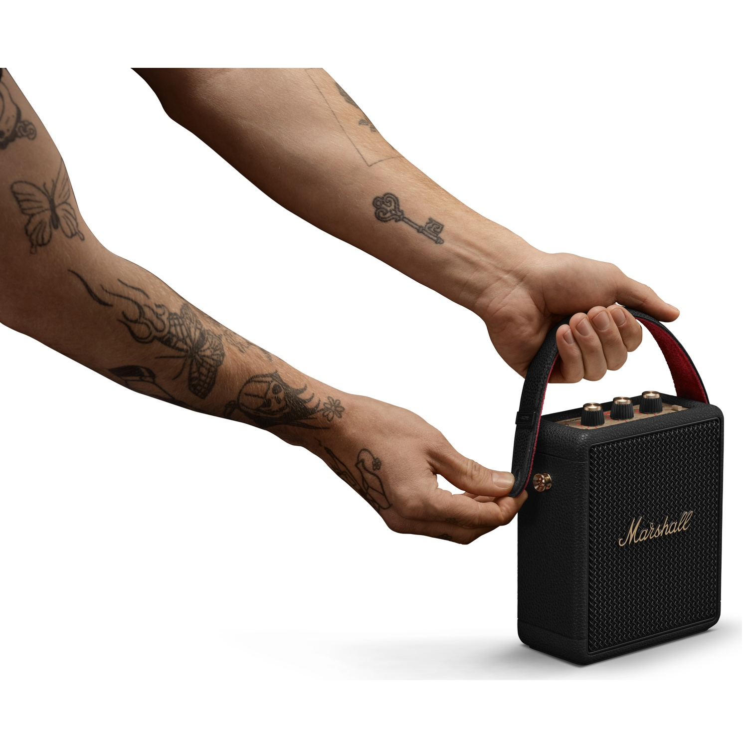Tattooed arms attach the red and black strap of a portable Marshall speaker.