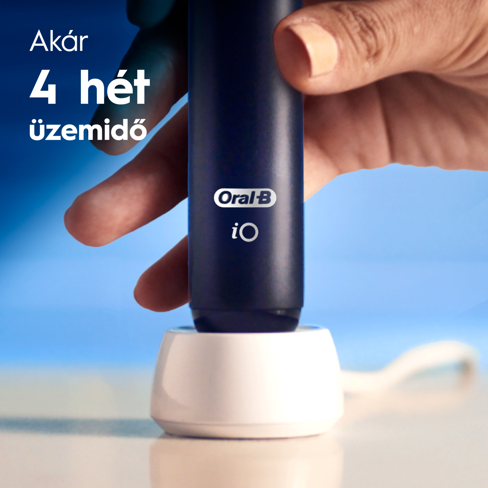 Egy kéz egy fekete Oral-B iO elektromos fogkefét tart egy fehér töltőalapon.