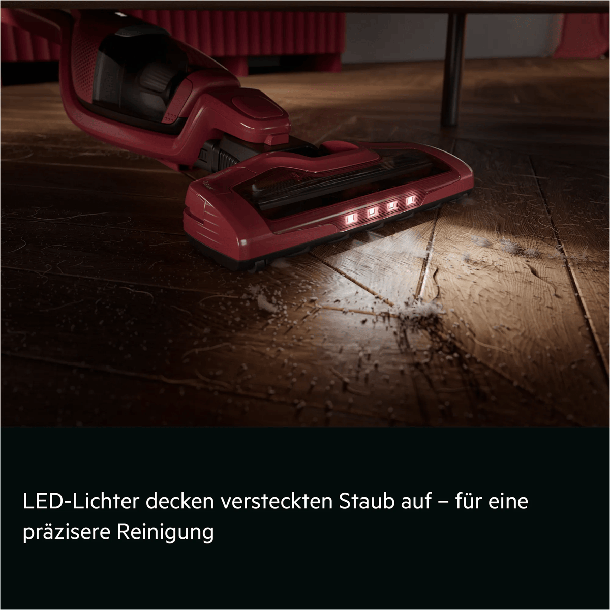 Roter Staubsauger mit integrierten LED-Leuchten reinigt präzise einen dunklen Holzfußboden.