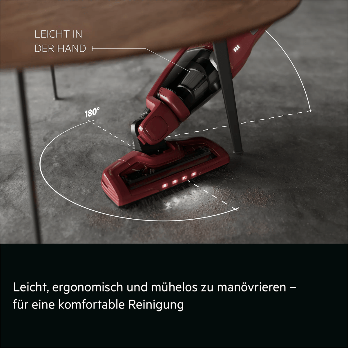 Ein roter Staubsauger reinigt unter einem Tisch mit 180-Grad-Drehung.