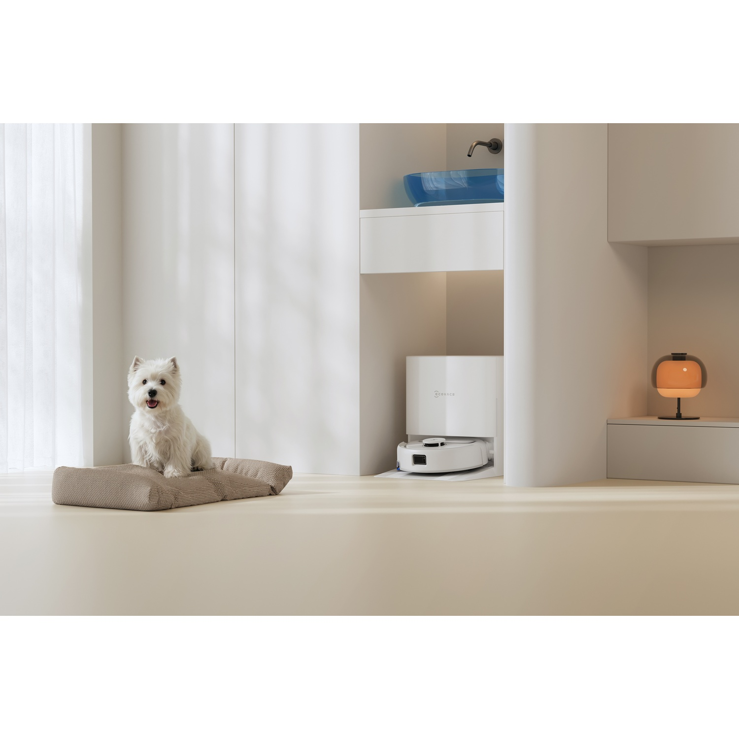 Un piccolo cane bianco siede su un cuscino vicino a un robot aspirapolvere in un interno moderno.