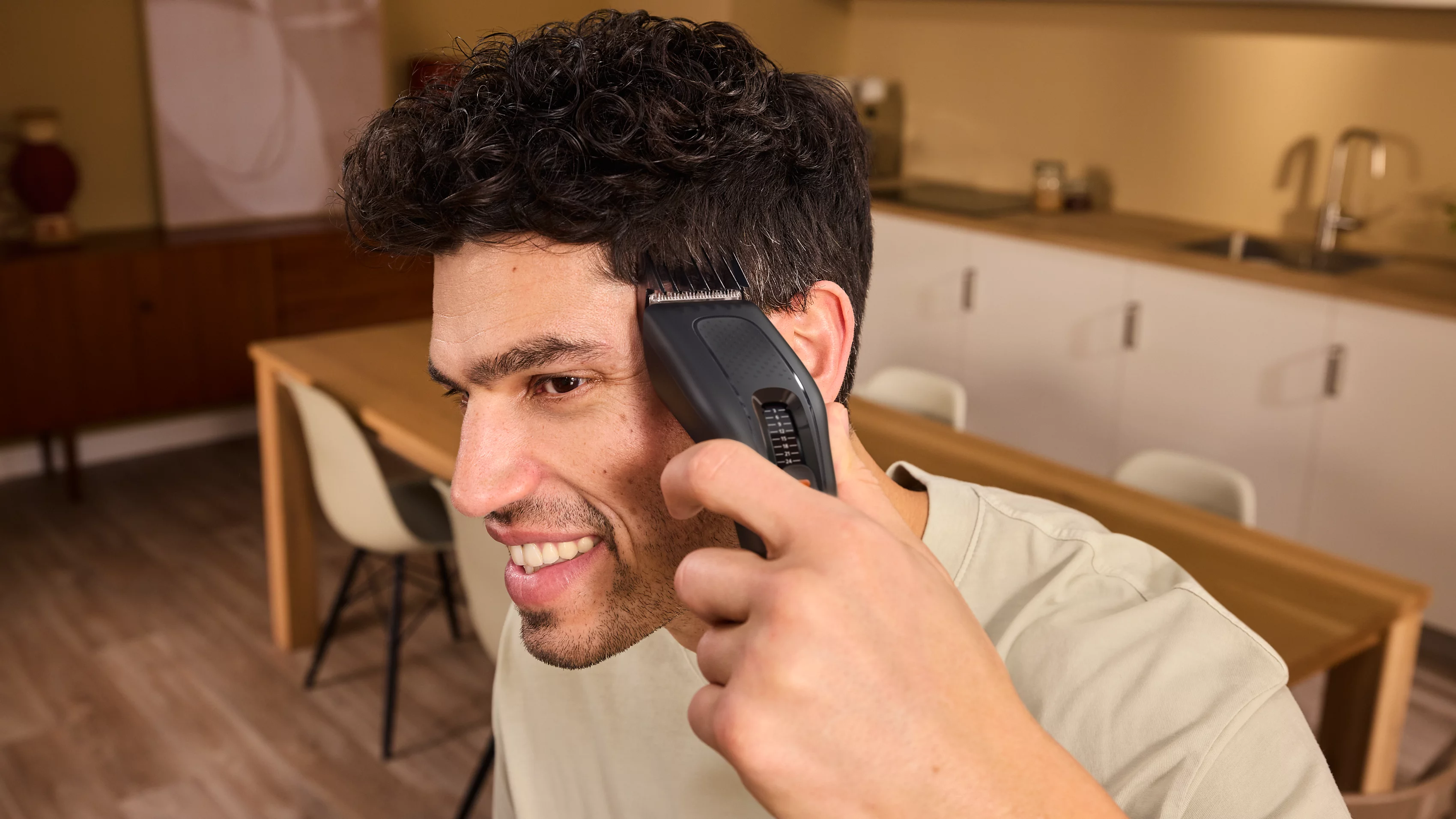 Ein Mann schneidet sich in einer Küche selbst die Haare mit einem elektrischen Trimmer.