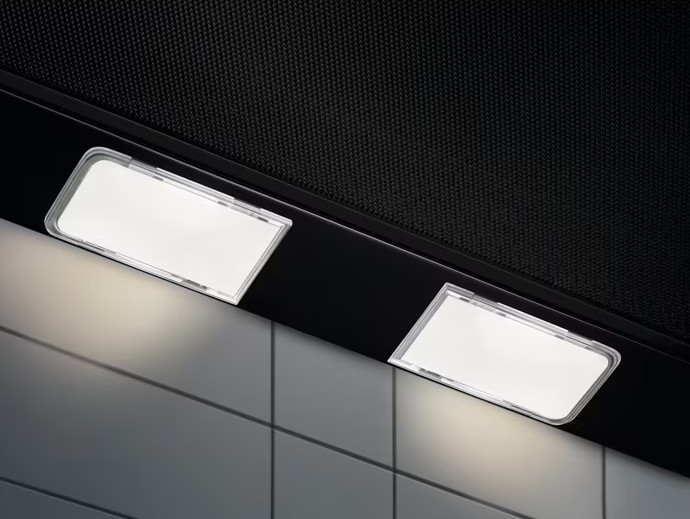 Dwie prostokątne lampki LED na czarnym okapie kuchennym nad białymi kafelkami.