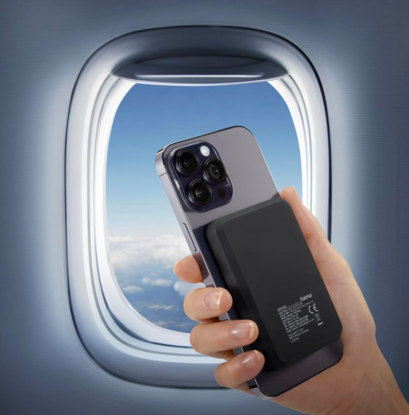 Handy mit angebrachter Powerbank vor einem Flugzeugfenster mit Wolkenblick.