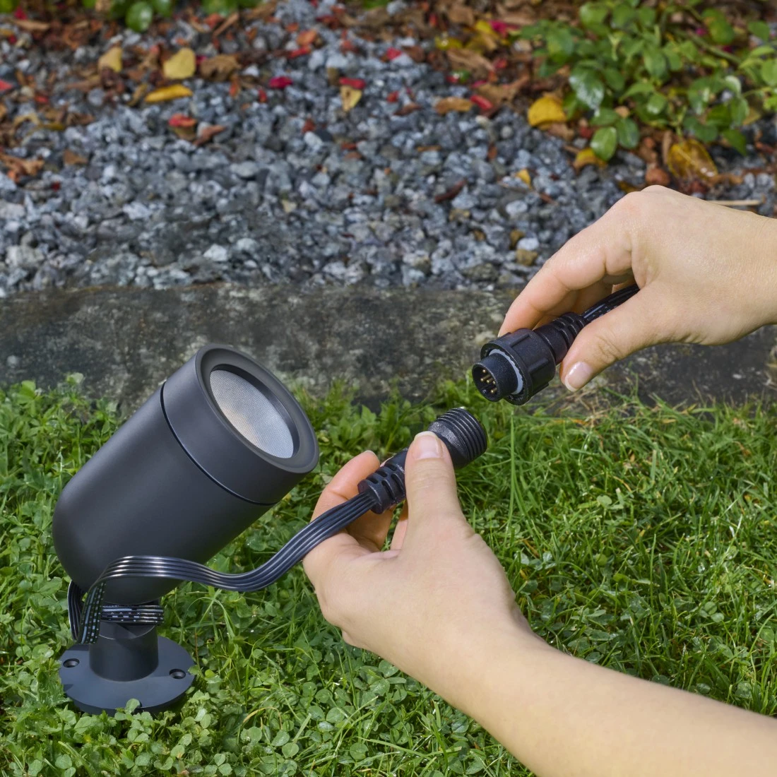 Hände verbinden die Kabel einer schwarzen Gartenlampe auf dem Rasen.
