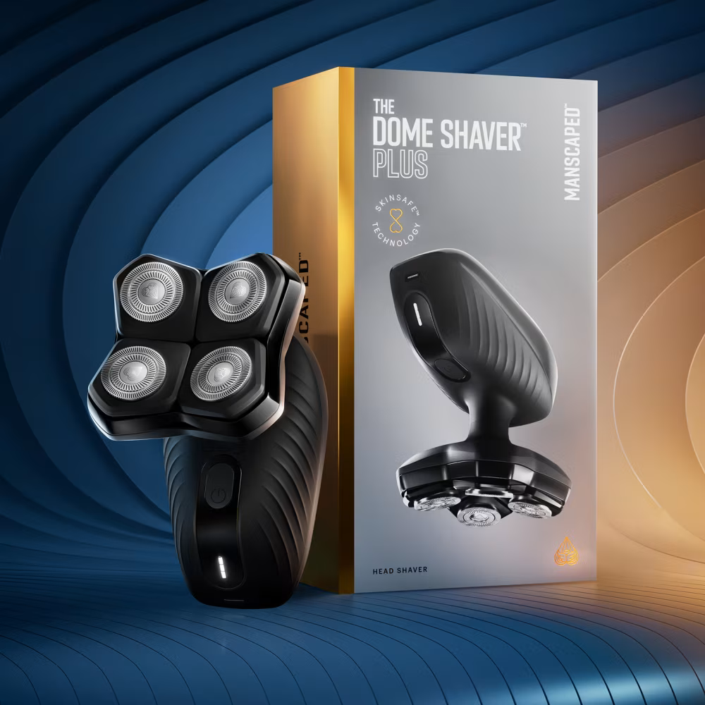 Ein schwarzer Dome Shaver Plus Rasierer steht vor seiner silbernen und goldenen Verpackung auf blauem Hintergrund.