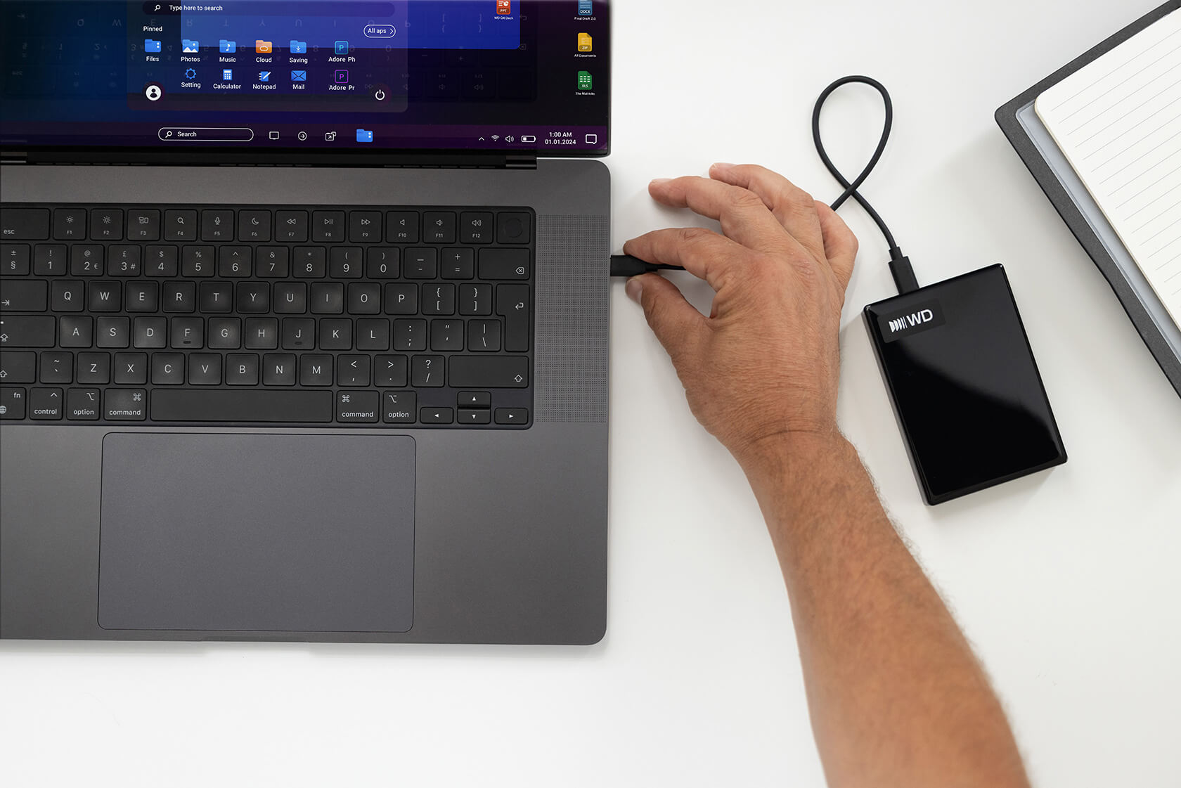Eine Hand verbindet eine externe Festplatte mit einem Laptop auf einem Tisch.