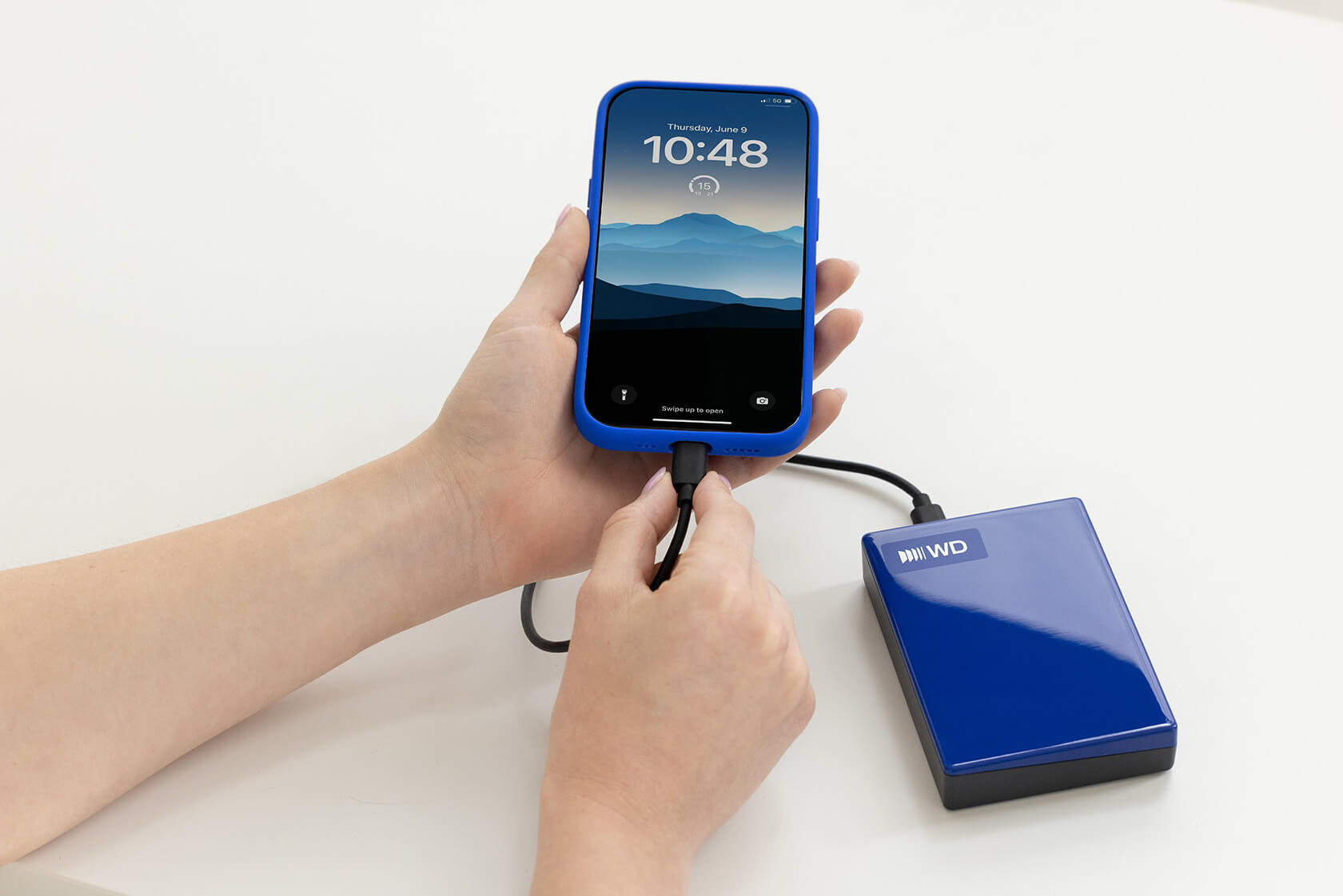 Eine Person verbindet ein blaues Smartphone mit einem blauen externen WD-Festplattenlaufwerk auf weißem Tisch.