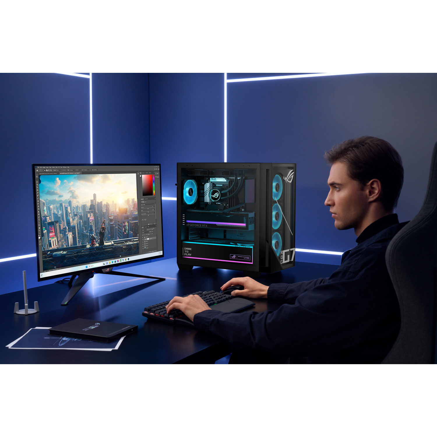 A man sits at a desk in front of a glowing PC tower, editing images on a large monitor in a blue-lit room.