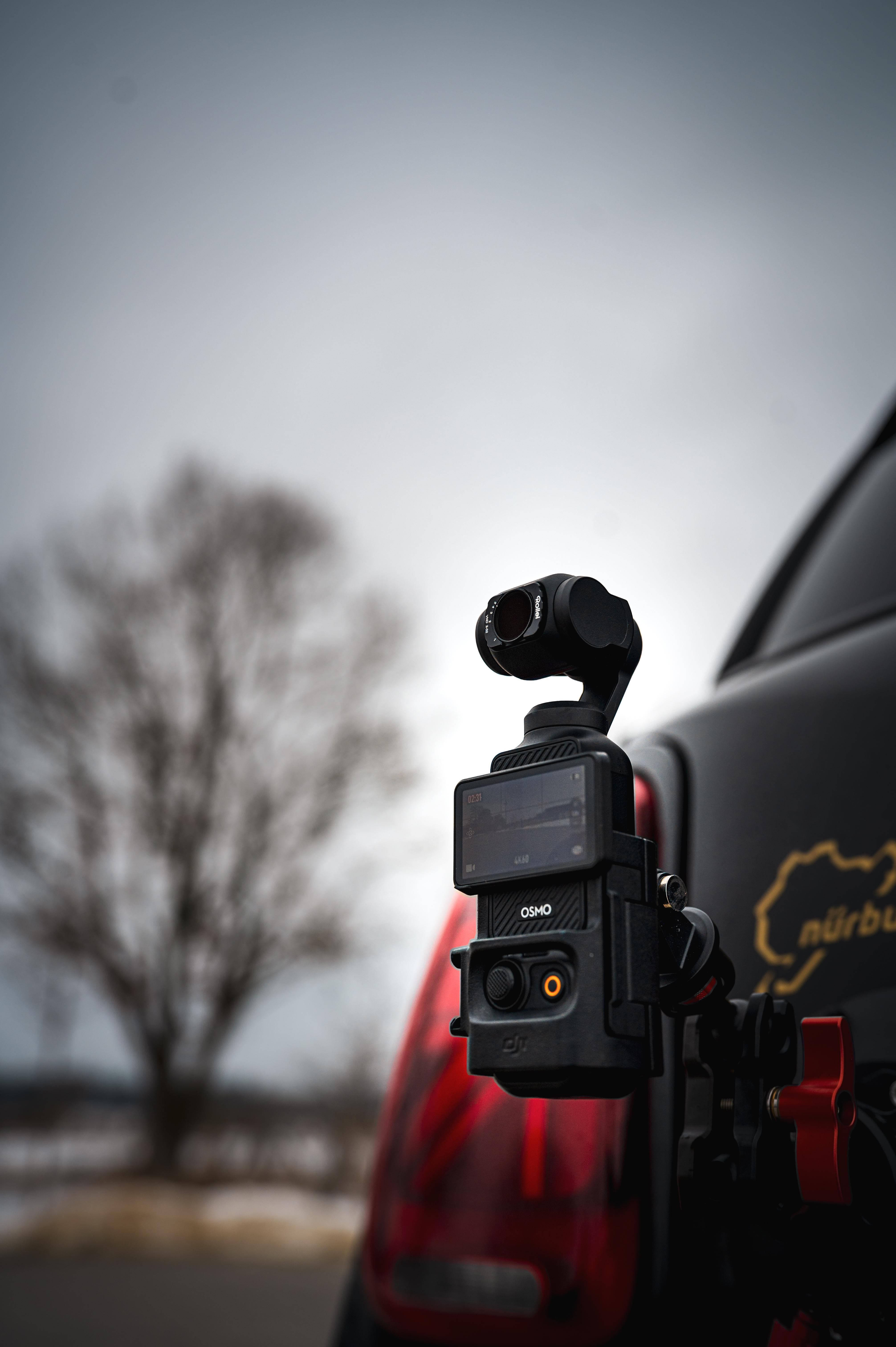 Eine schwarze DJI Osmo Action-Kamera ist an der Rückseite eines Autos montiert, im Hintergrund ein kahler Baum.