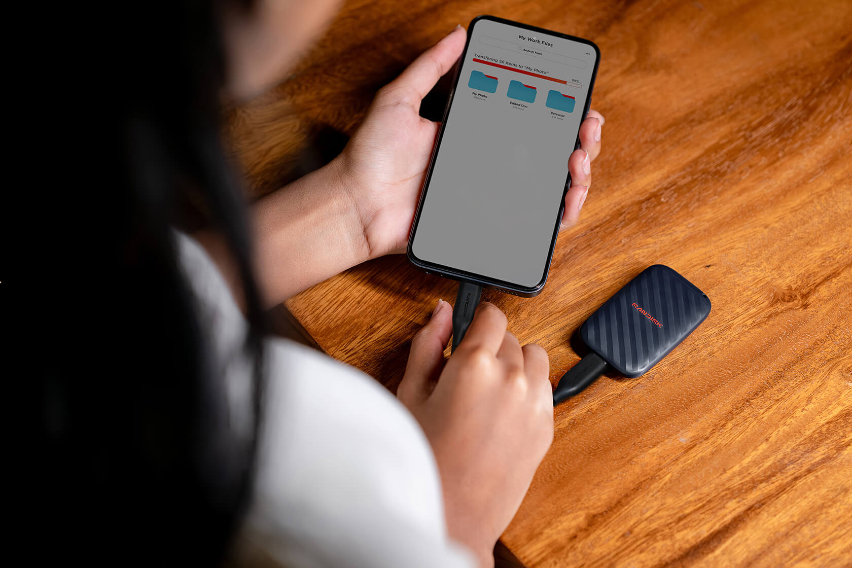 Person verbindet ein Smartphone mit einem externen Solid-State-Laufwerk auf einem Holztisch.