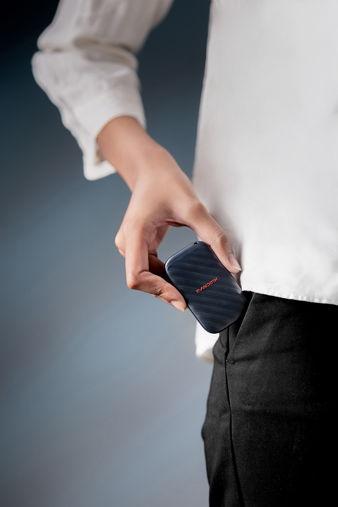 Eine Person steckt eine kleine schwarze SanDisk SSD in ihre Hosentasche.