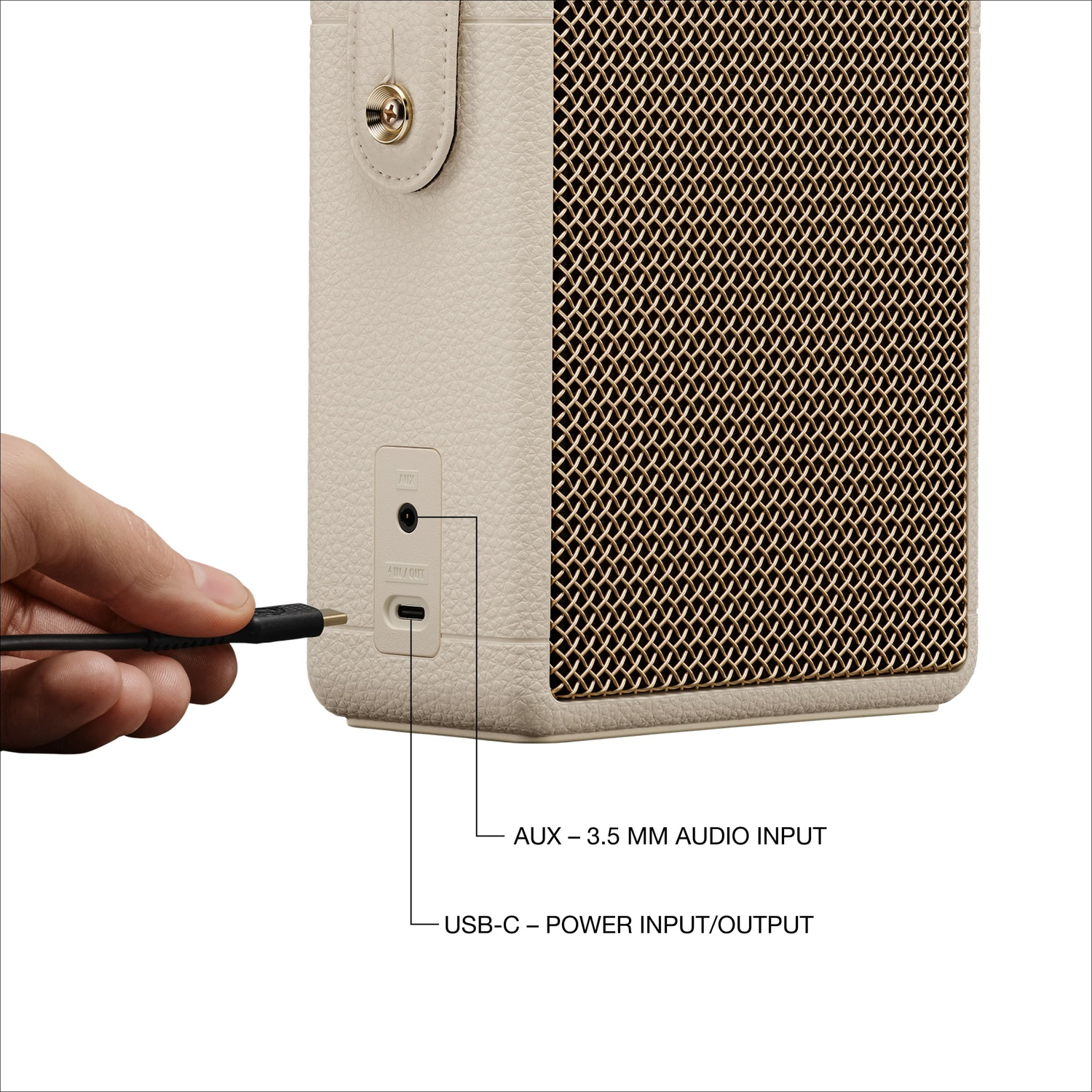 A hand connects a USB-C cable to the bottom of a cream speaker with AUX and USB-C ports.