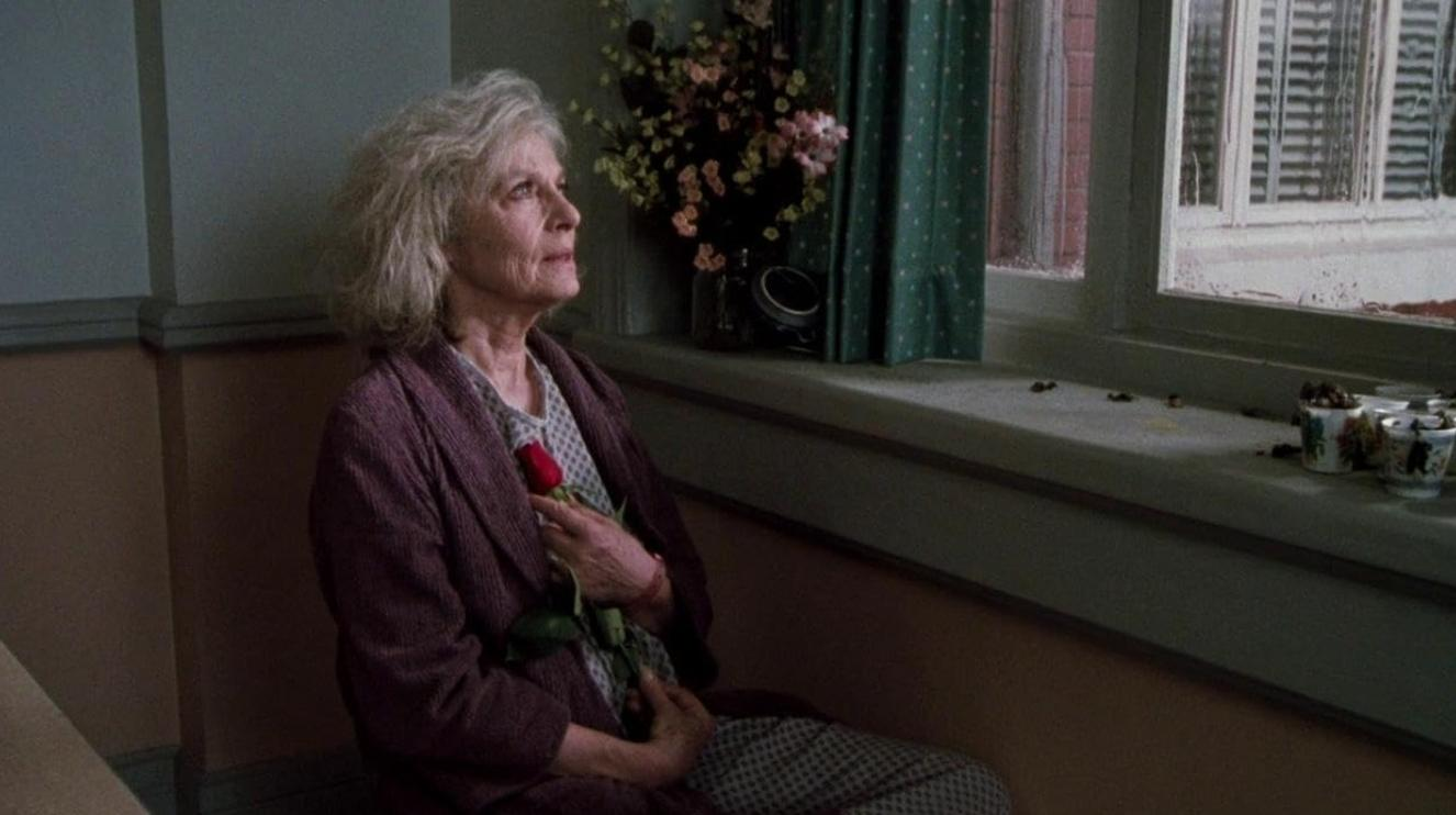 Eine ältere Frau sitzt im Zimmer und hält eine rote Rose.