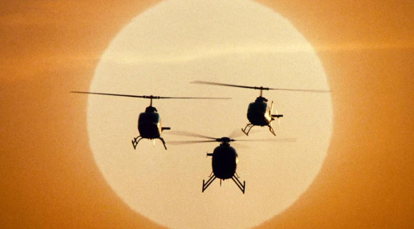 Drei Hubschrauber fliegen in Formation vor einem großen, hellen Abendhimmel.