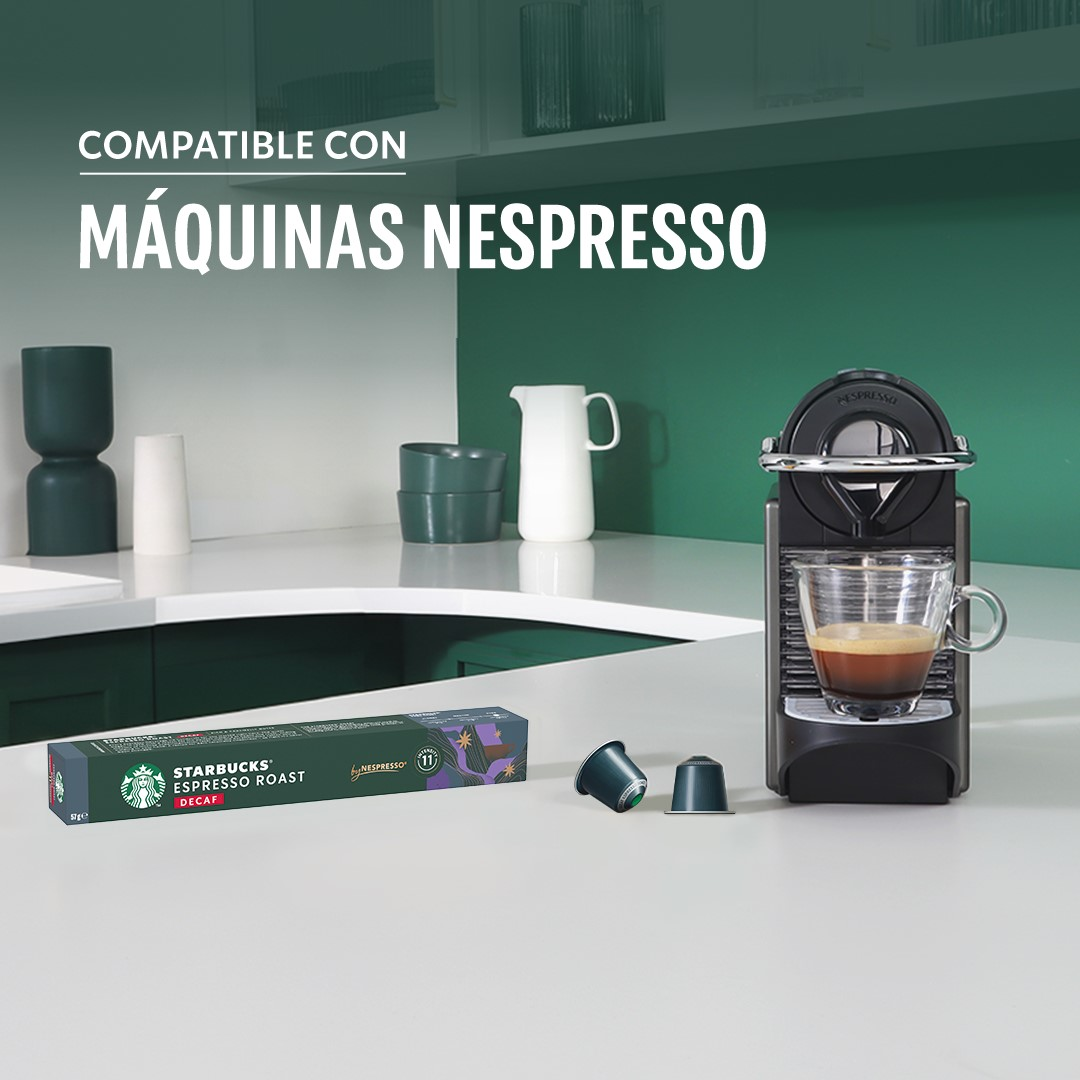 Una cafetera negra con una taza de espresso de cristal está en una encimera de cocina junto a cápsulas.