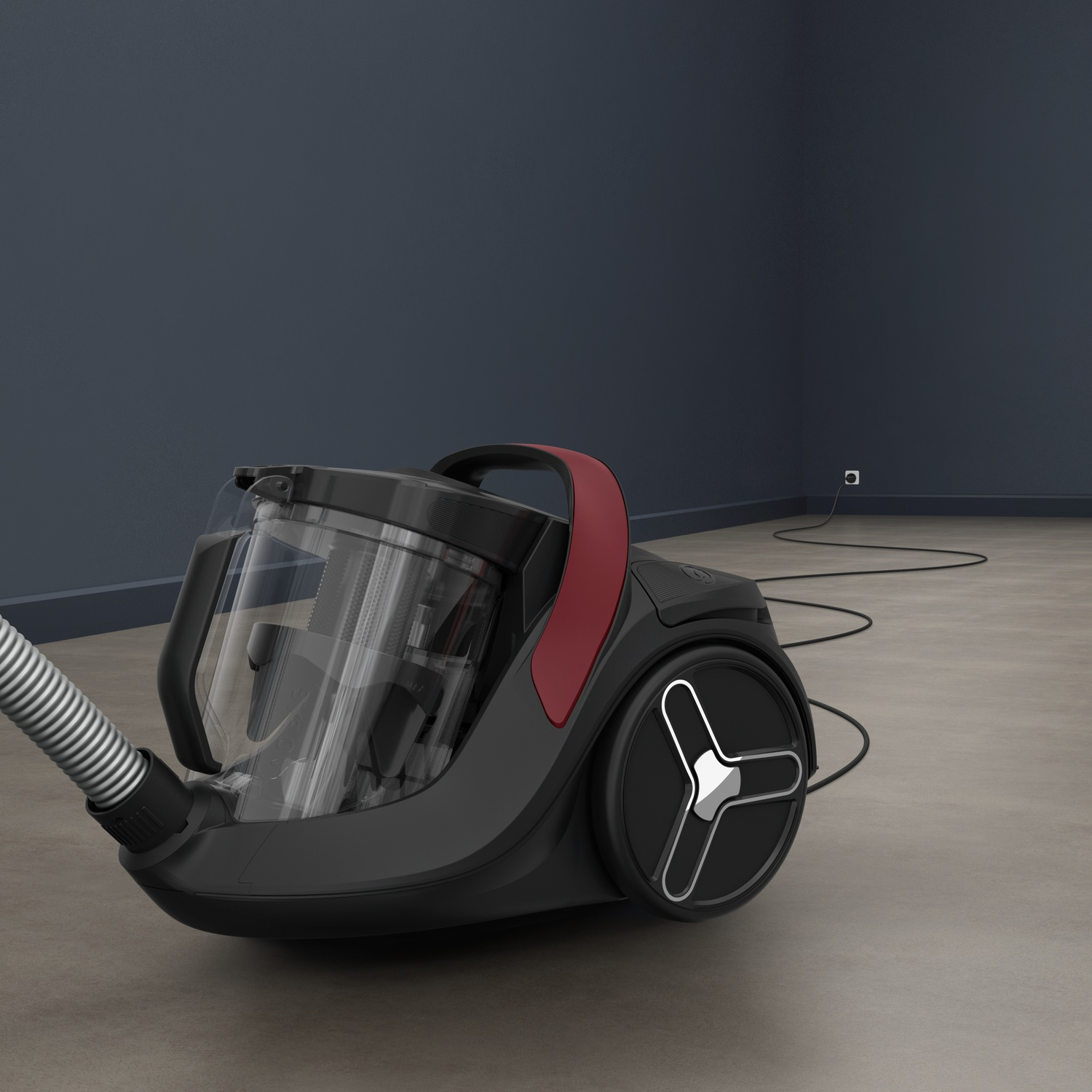 A black and red bagless vacuum cleaner on a concrete floor in a room with dark blue walls.