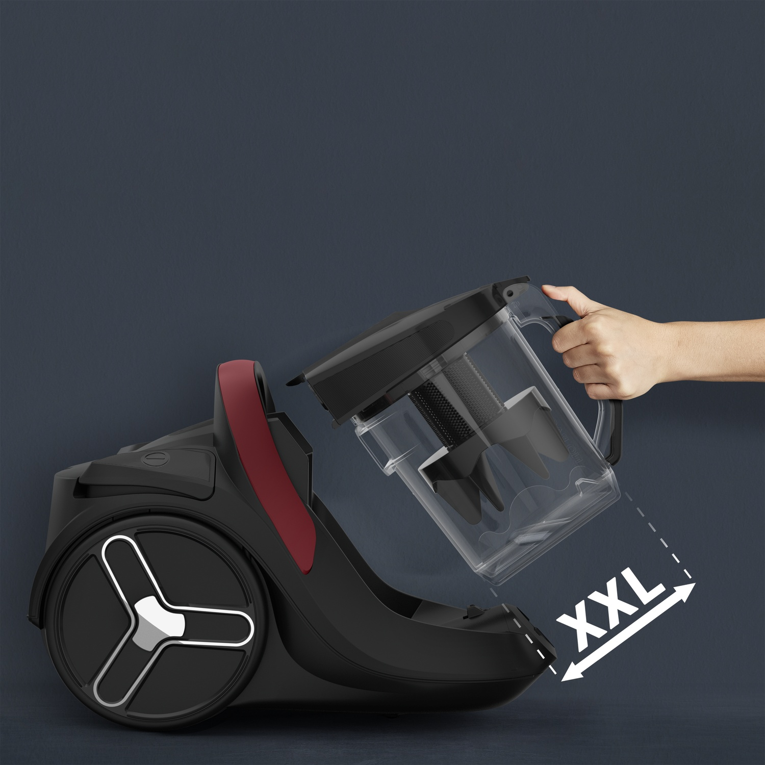 A hand attaches an XXL dust container to a black vacuum cleaner.