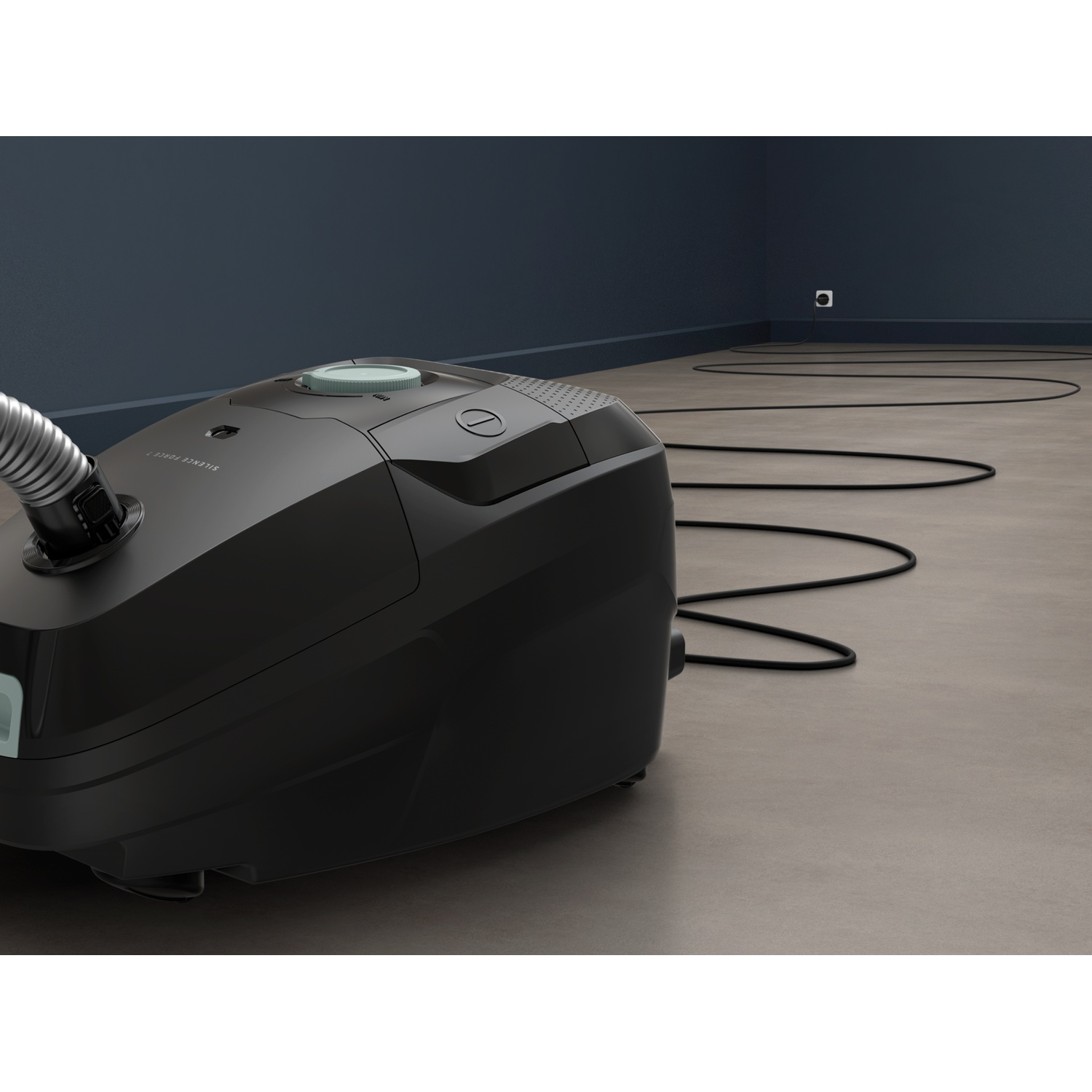 A black vacuum cleaner stands on a floor, its cord snakes towards a wall outlet on the blue wall.