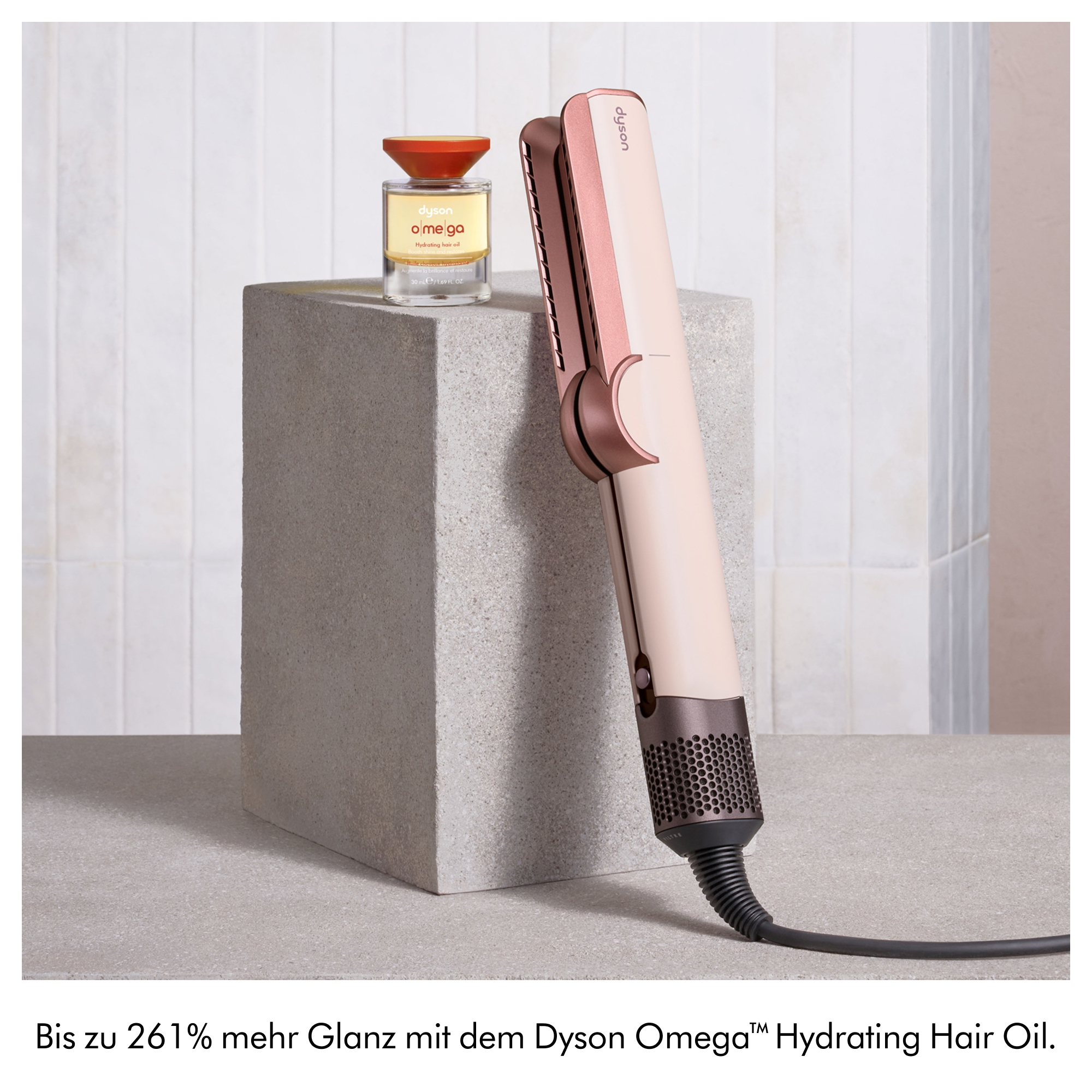 Ein Dyson Airstrait Haarglätter und eine Flasche Dyson Omega Hydrating Hair Oil stehen auf einem grauen Block.
