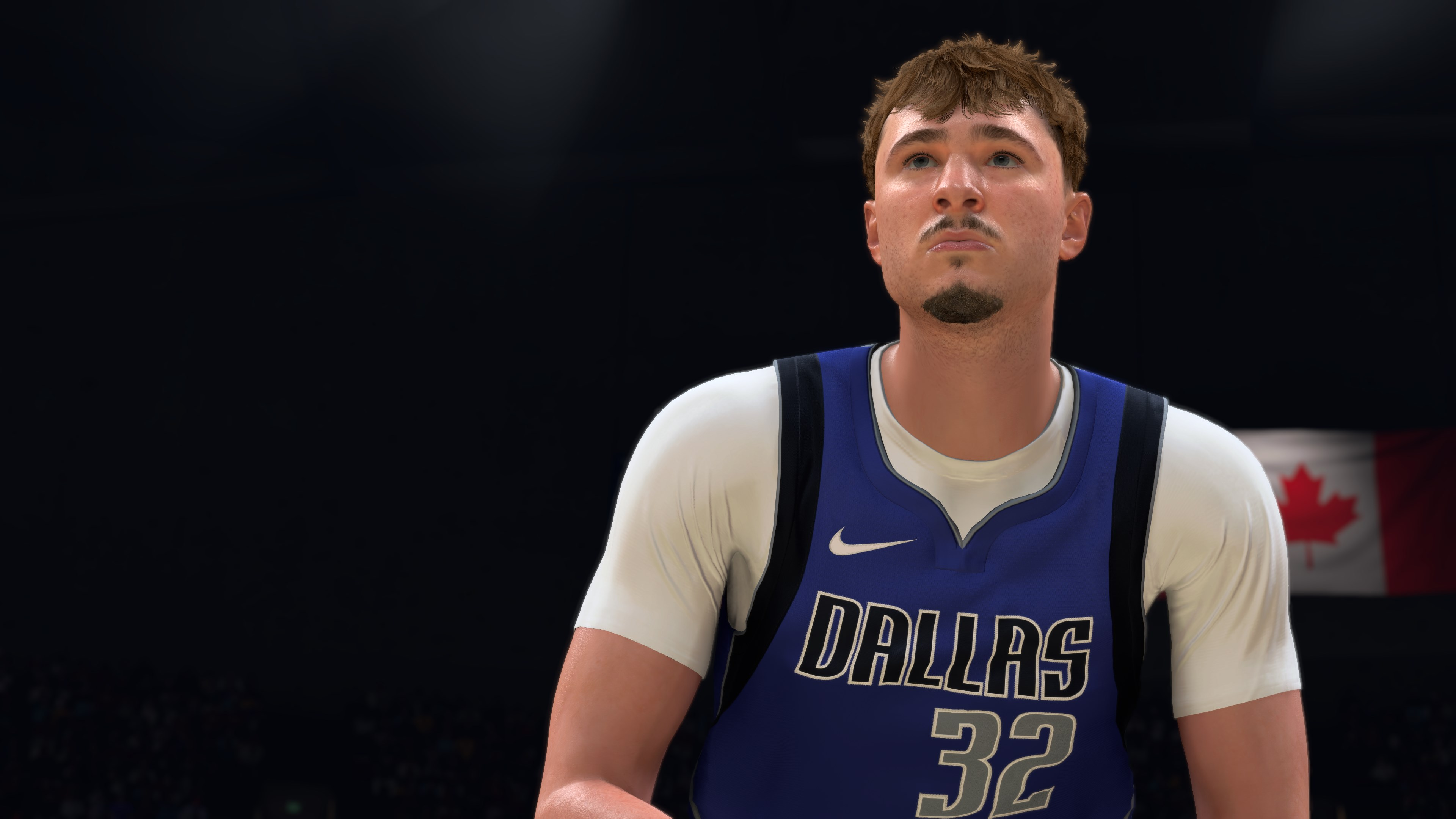 Un giocatore di basket con una maglia blu dei Dallas guarda in alto in un'arena buia.