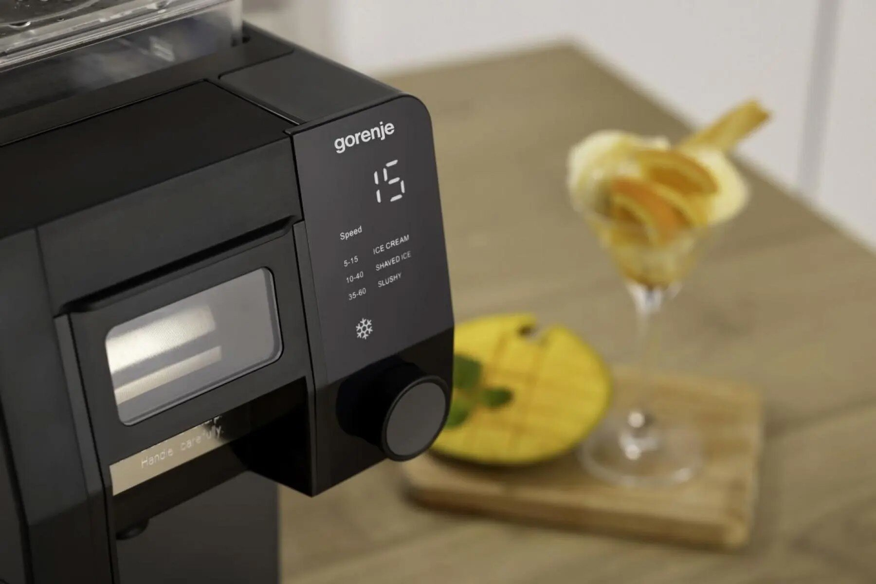 Czarne urządzenie kuchenne Gorenje z cyfrowym wyświetlaczem na drewnianym blacie obok deseru i mango.