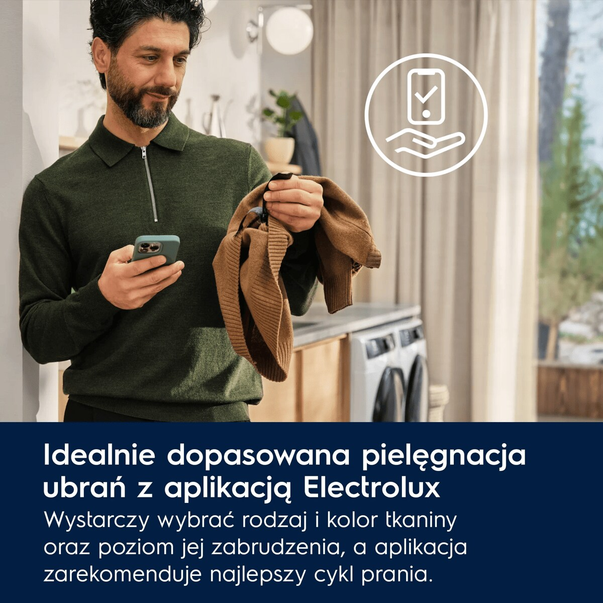 Mężczyzna w zielonym swetrze trzyma smartfon i brązową część garderoby. W tle pralki i tekst.