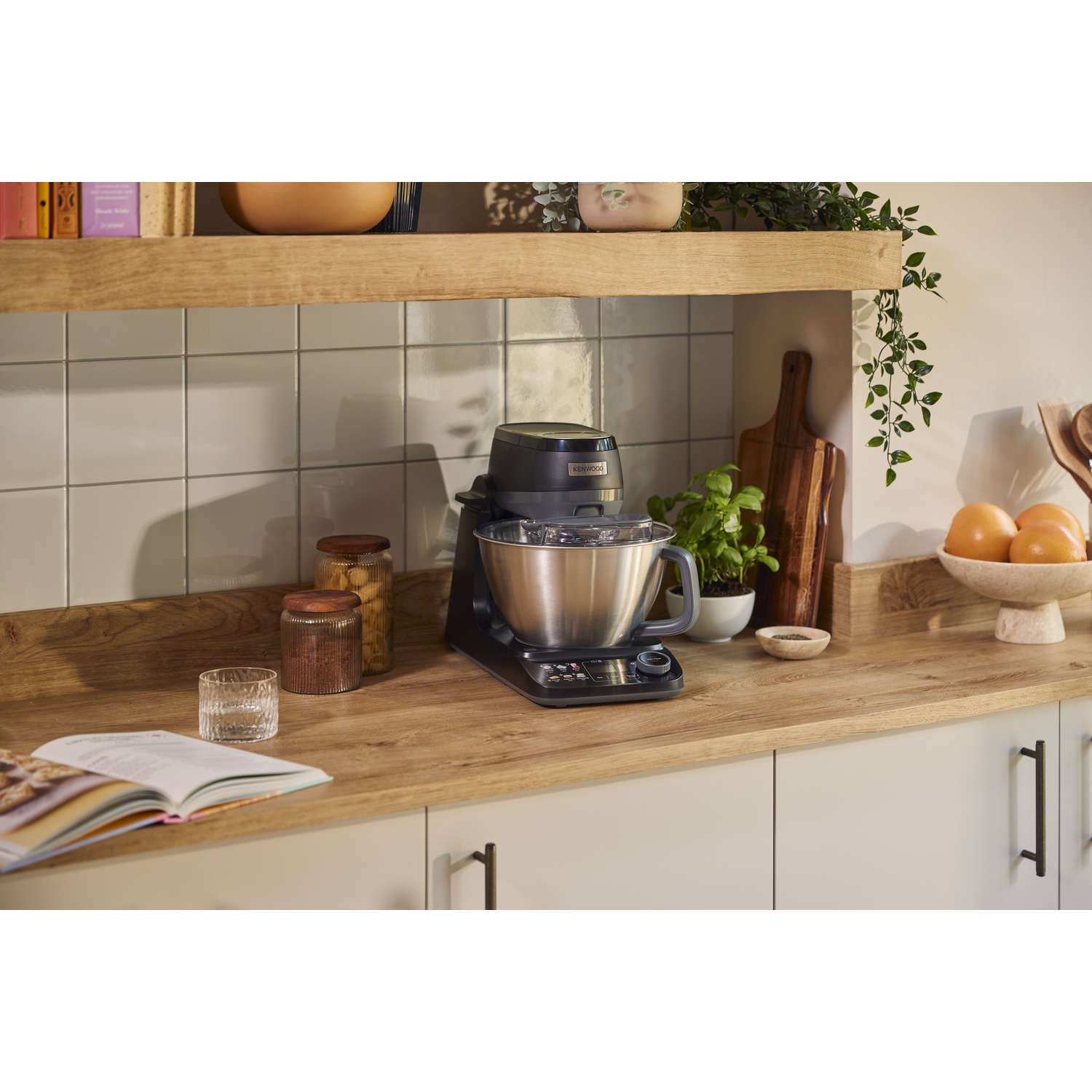 Een grijze keukenmachine met RVS kom staat op een houten aanrechtblad in een keuken.