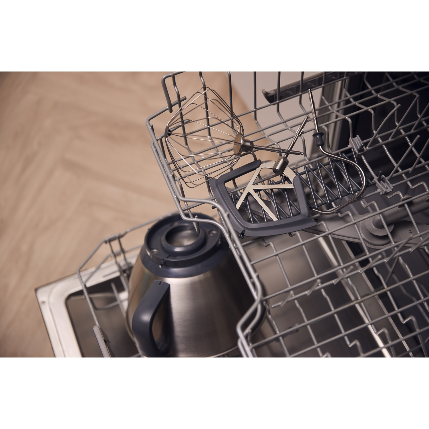 Vaatwasser geladen met keukenmachine-opzetstukken en een roestvrijstalenkom op de rekken.