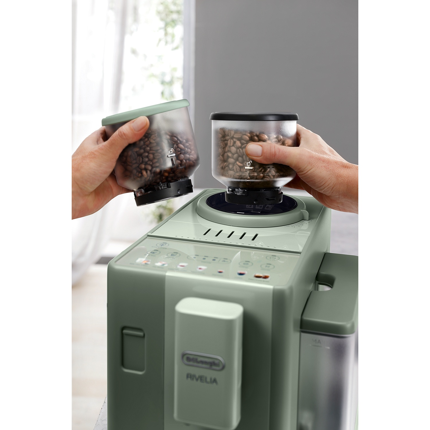 Handen wisselen de bonencontainer op een groene Delonghi Rivelia koffiemachine.
