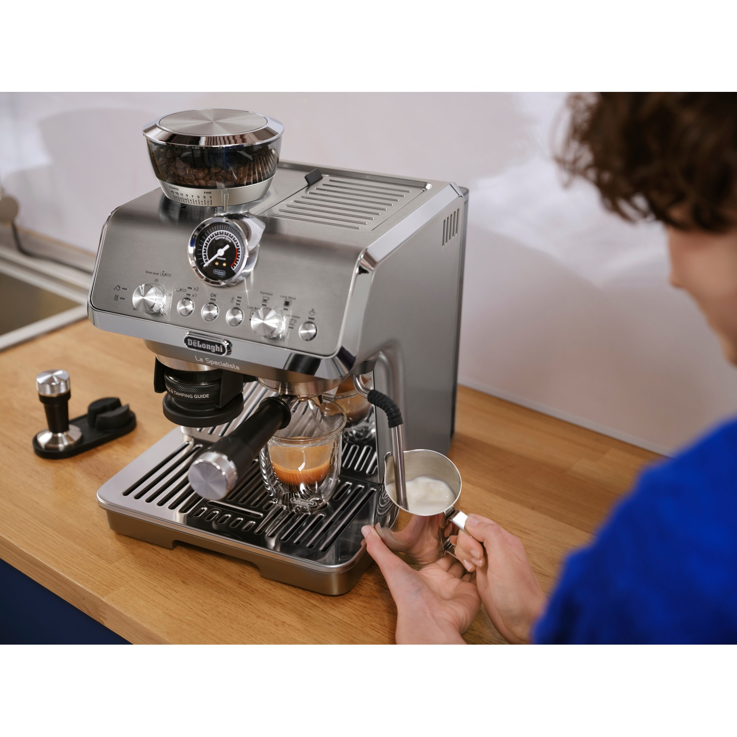 Een persoon schuimt melk op met een roestvrijstalen espressomachine op een houten blad.