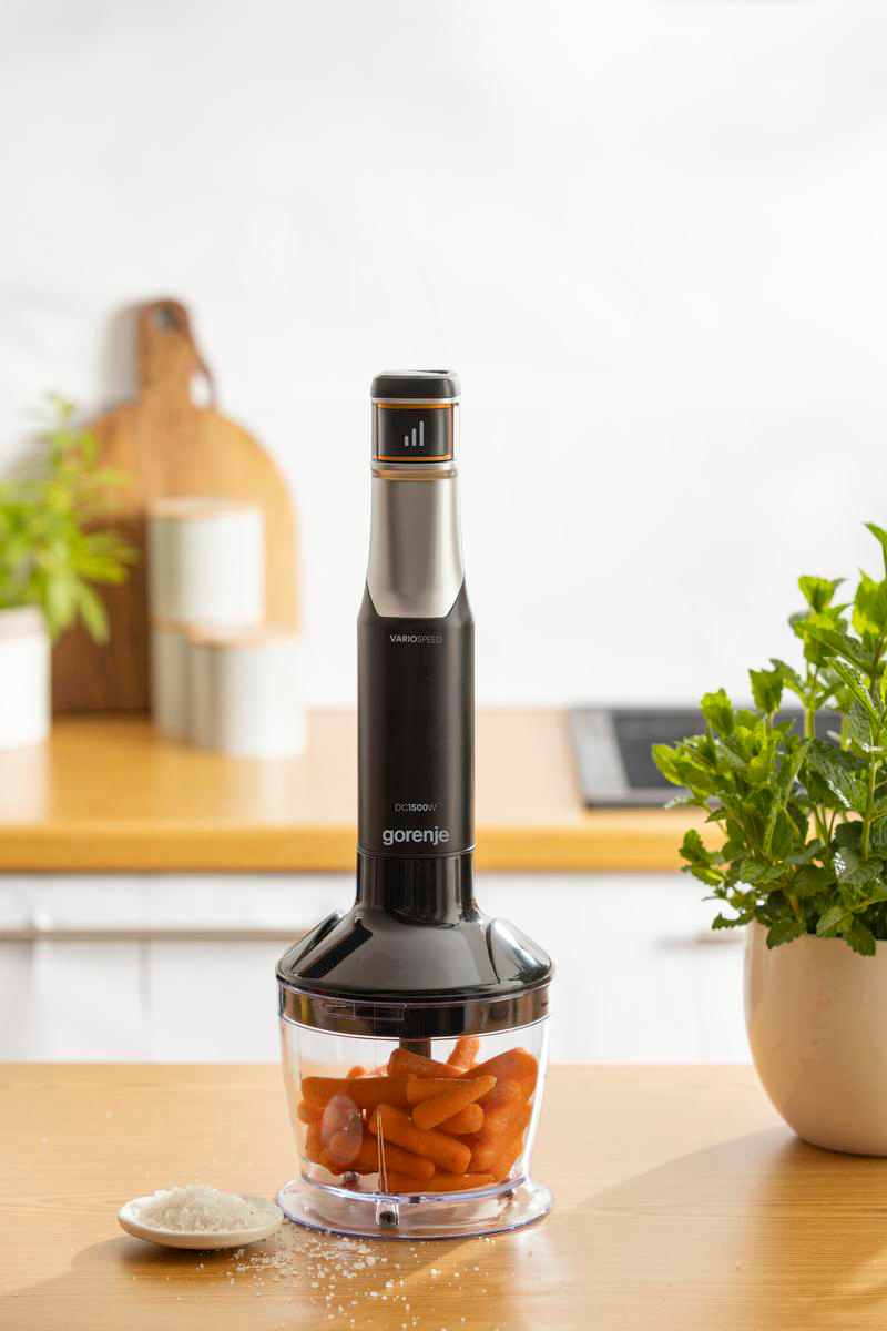 Ein Gorenje-Stabmixer mit Karotten im Becher steht auf einer Holzarbeitsplatte in der Küche.