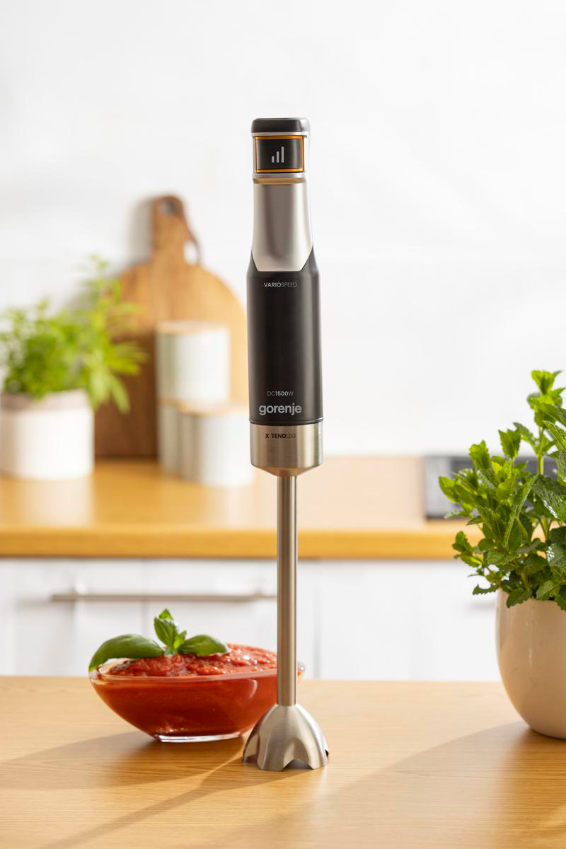 Ein Gorenje Stabmixer steht auf einer Holzarbeitsplatte neben einer roten Sauce und Pflanzen.