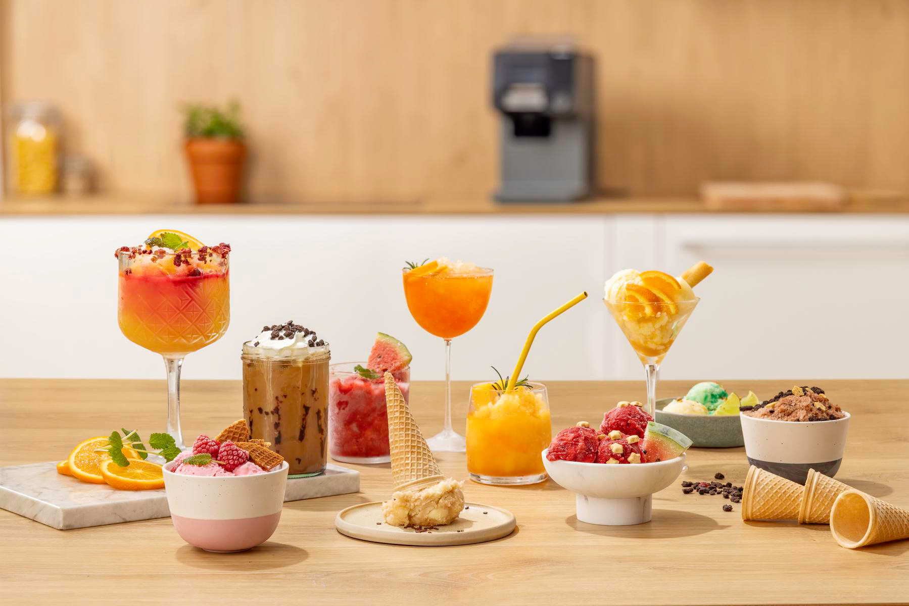 Ein Holztisch mit bunten Cocktails, Eiskaffee, Eisschalen und Waffeltüten.