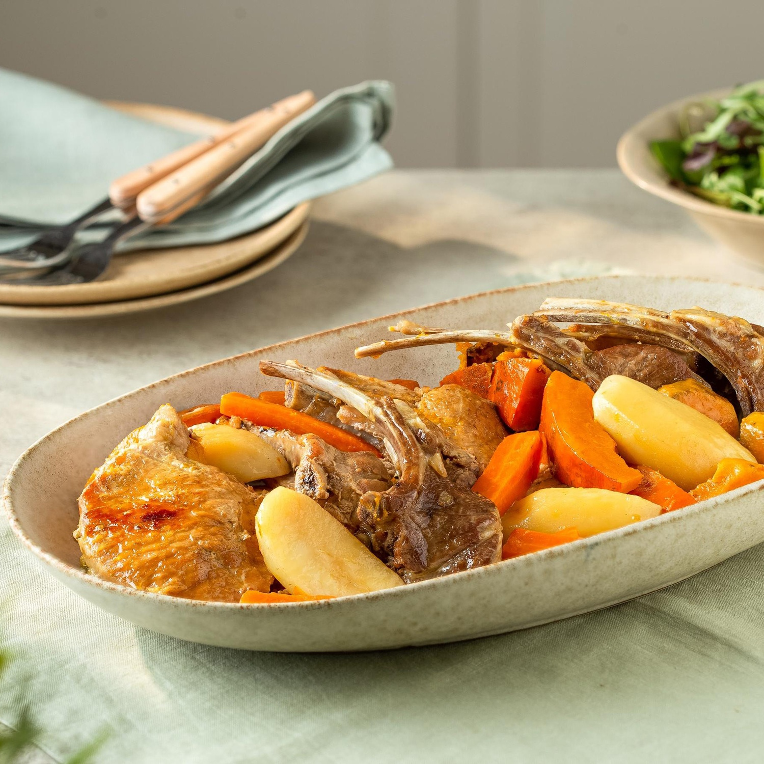 Roasted lamb chops with carrots and potatoes in an oval dish on a table.