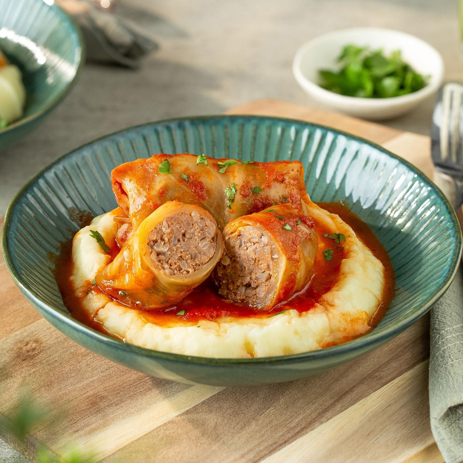Stuffed cabbage rolls in tomato sauce resting on mashed potatoes in a green bowl.