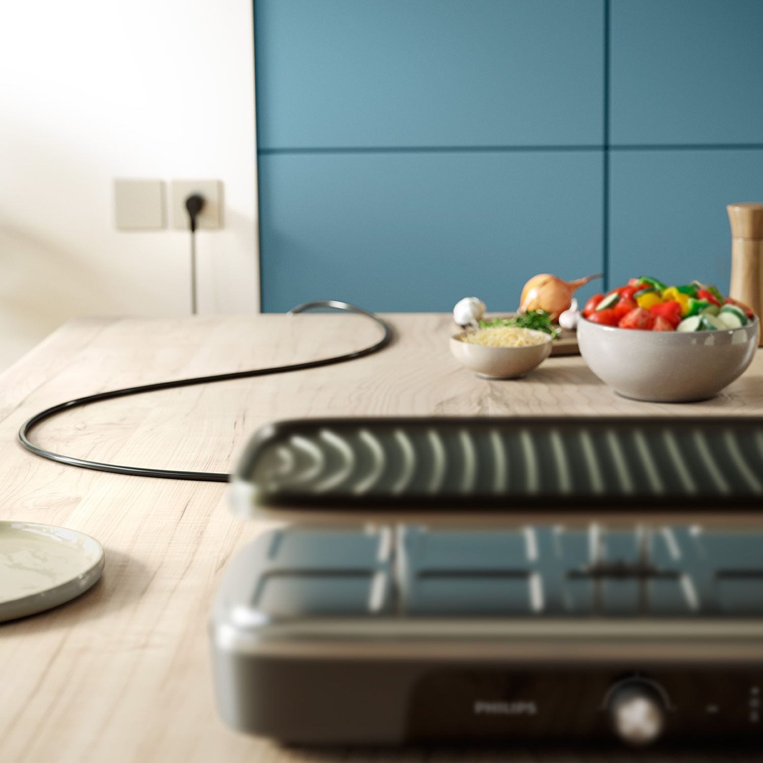 An electric tabletop grill rests on a wooden countertop in a modern kitchen with vegetables in the background.