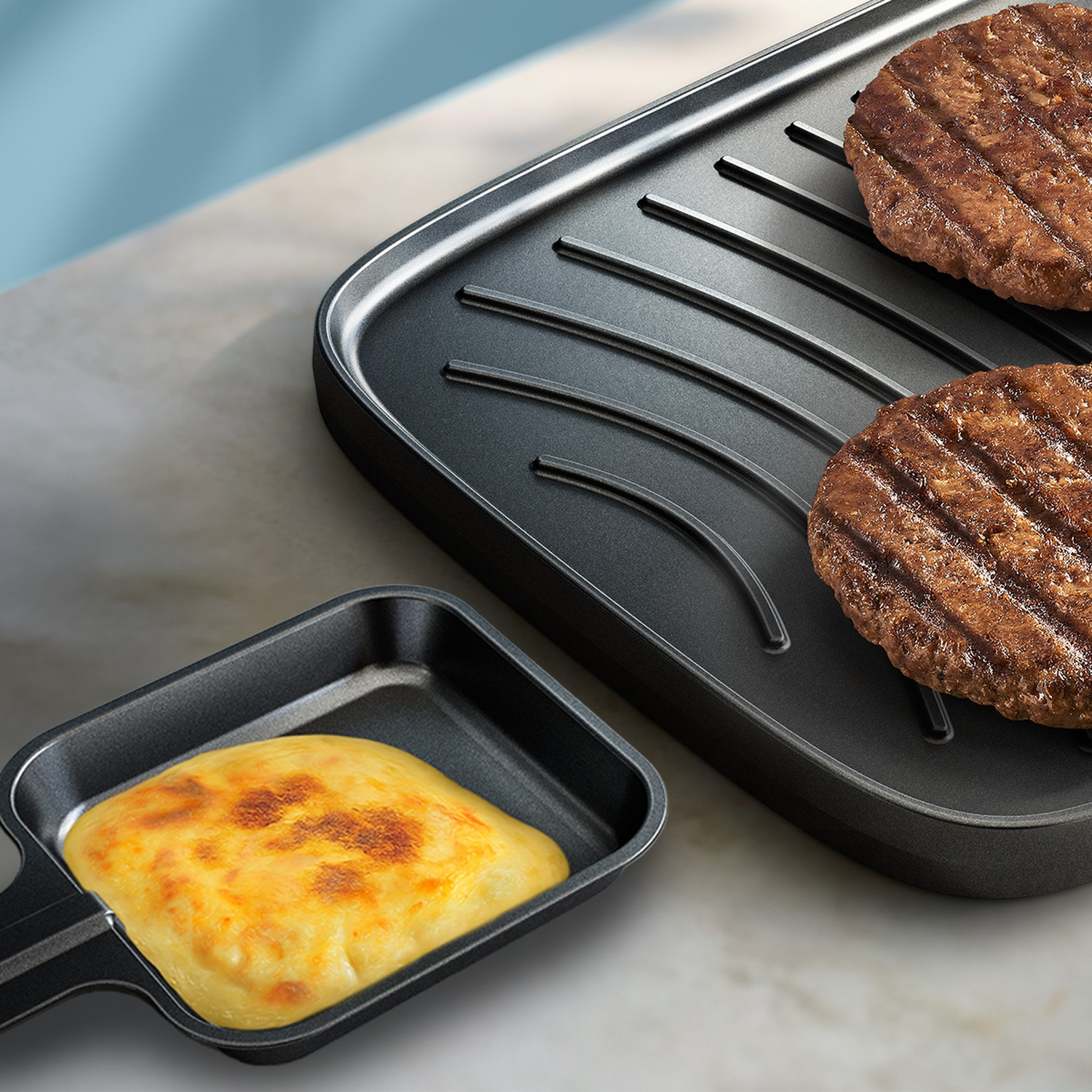 Two burger patties cooking on a black grill pan next to melted cheese in a small pan.