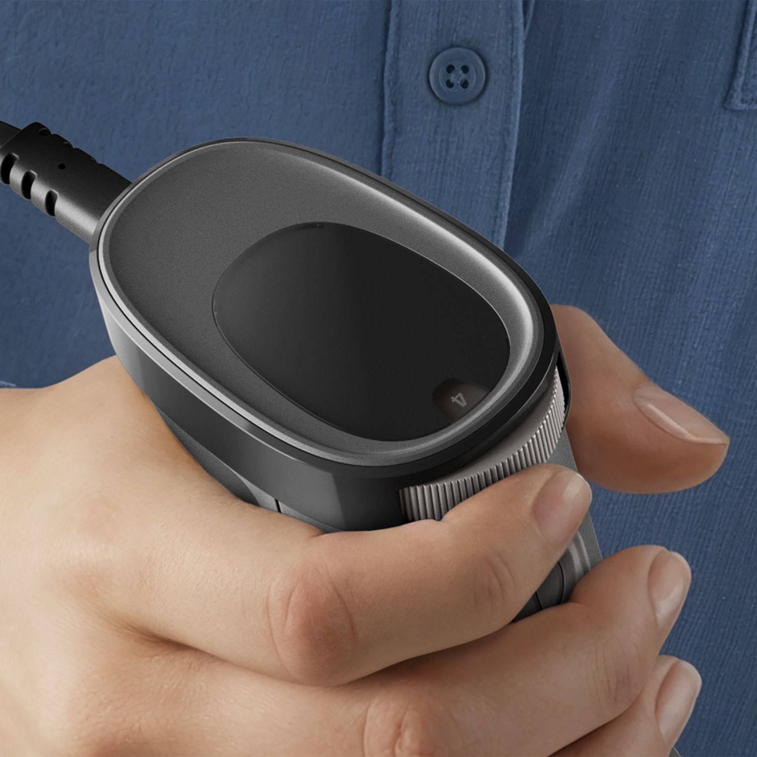 A hand holds a black, oval electronic device with a cable attached.